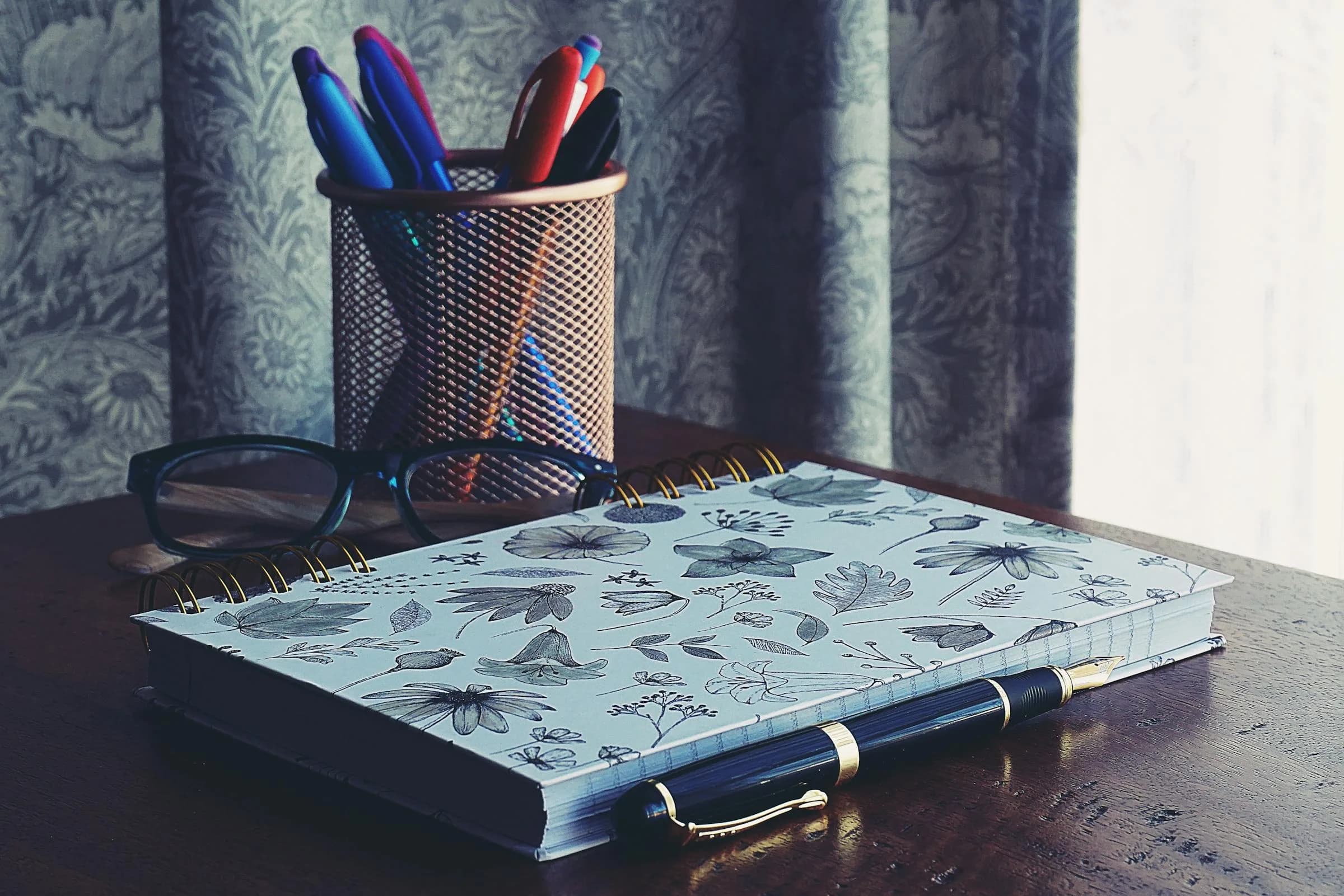 A tidy desk workspace with a notebook, glasses, and pens, suggesting manual note-taking alternatives