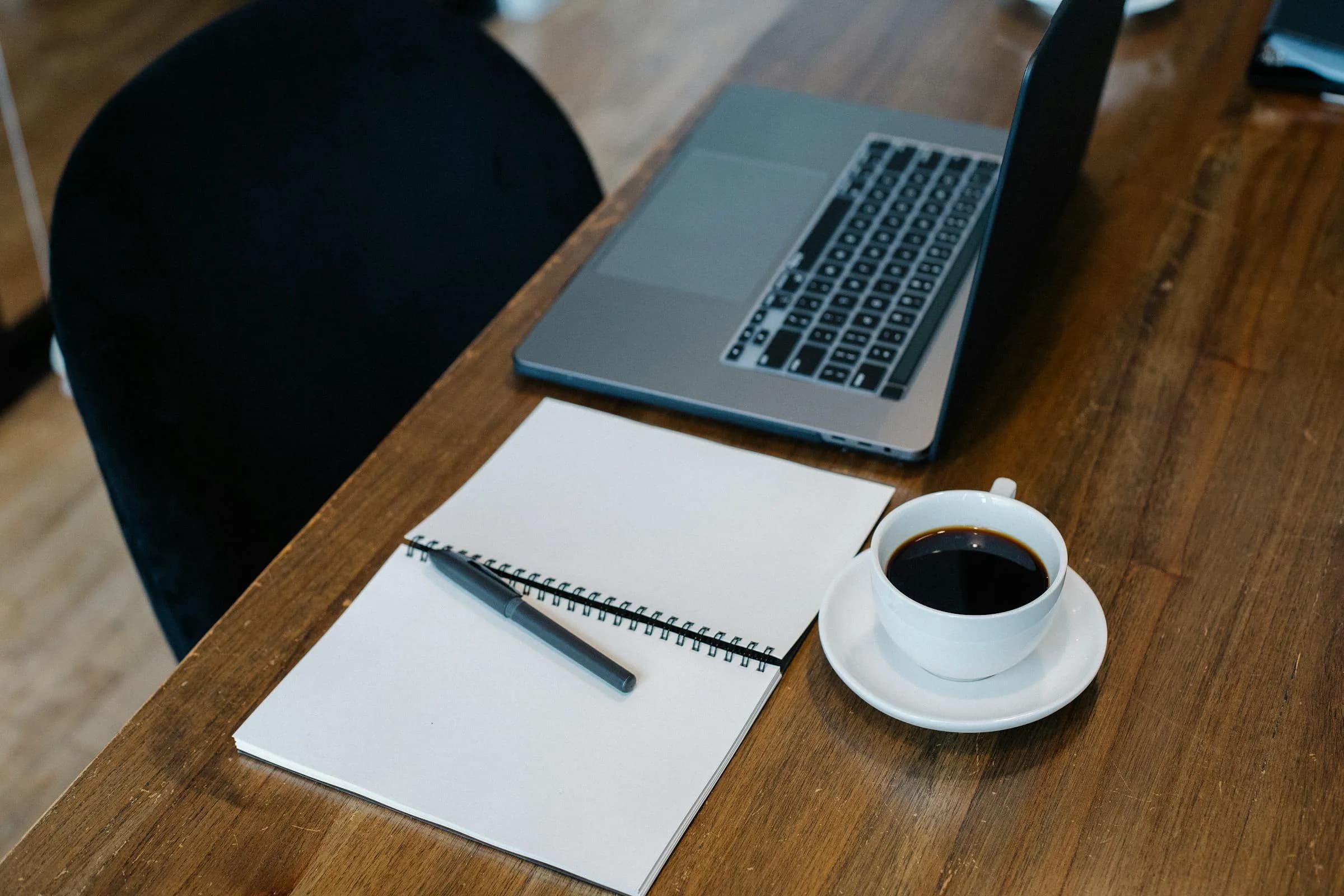 Laptop, open notebook and pen on a wooden desk, a setup for capturing voice notes as text