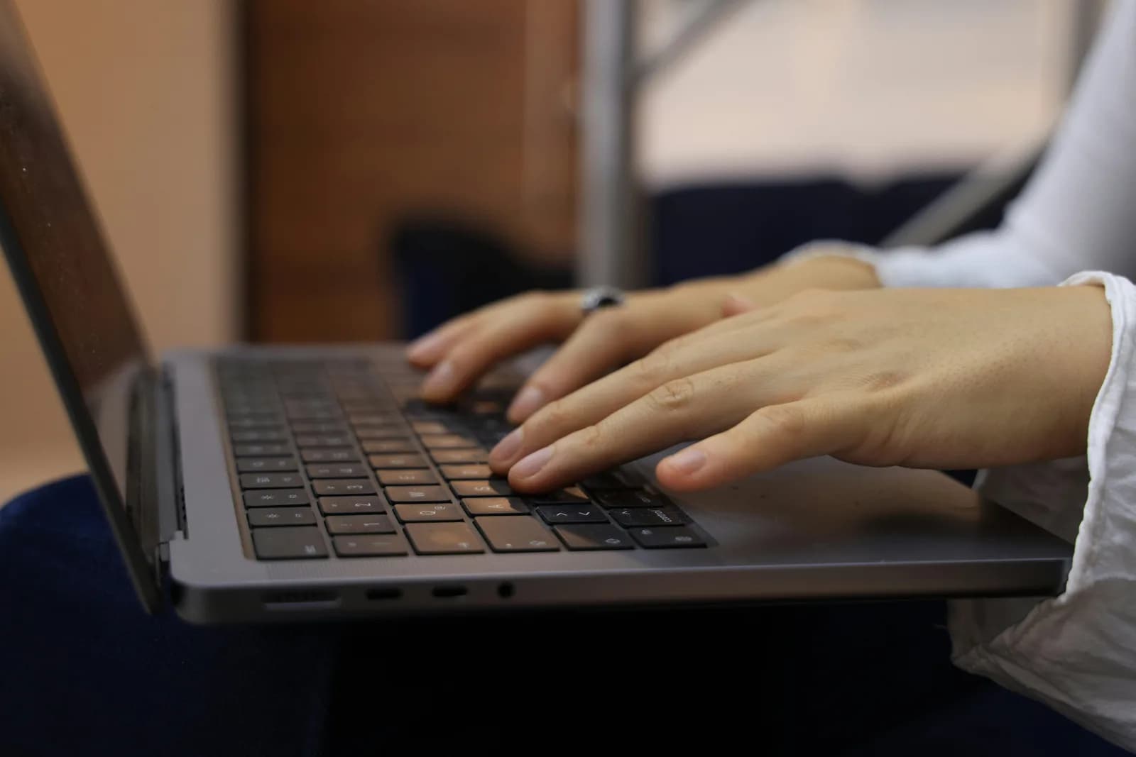 Hands typing on a laptop keyboard indoors, a plain writing workflow without a full assistant app