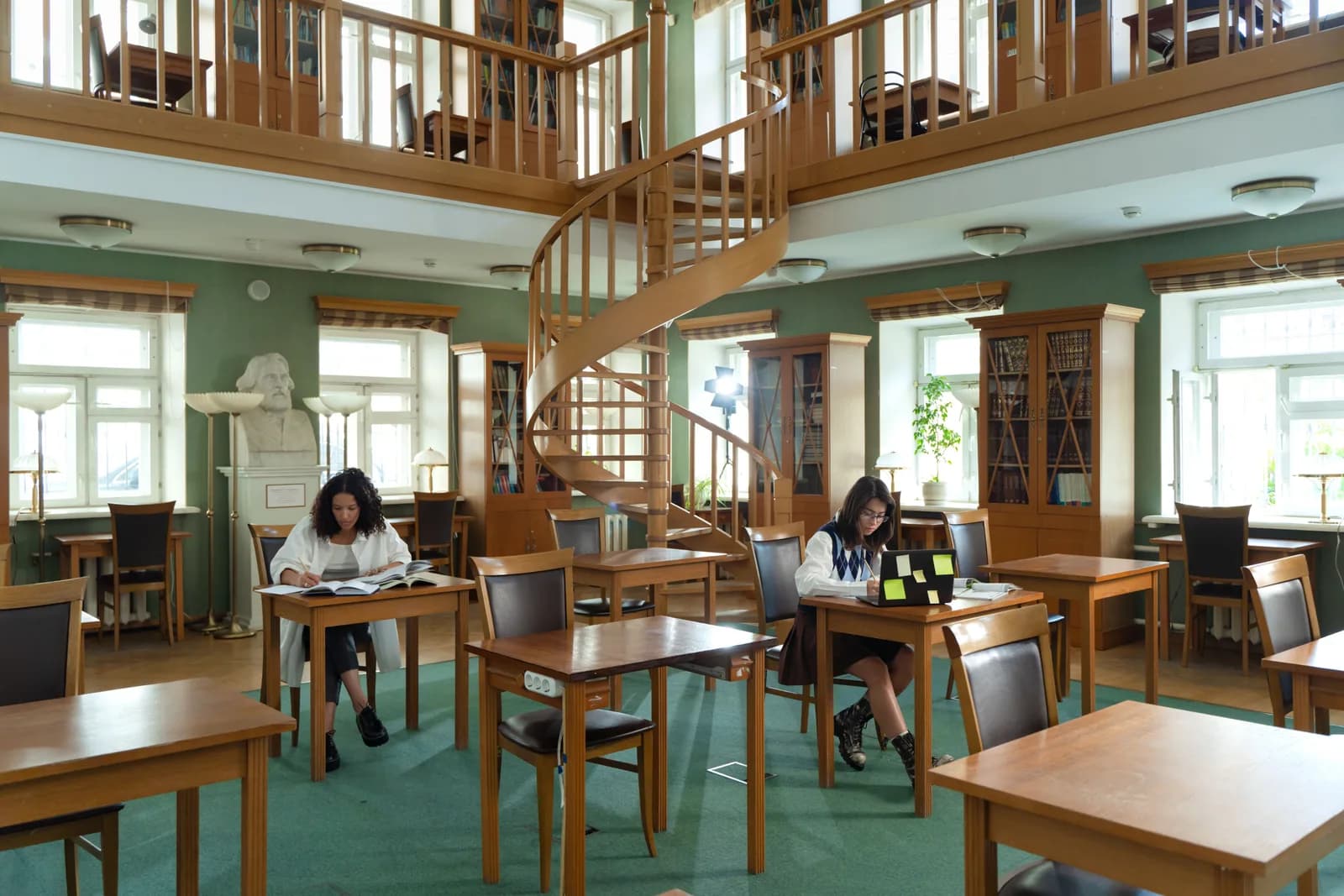 Quiet library reading room with stacked books and a laptop on a wooden desk, evoking research and academic writing