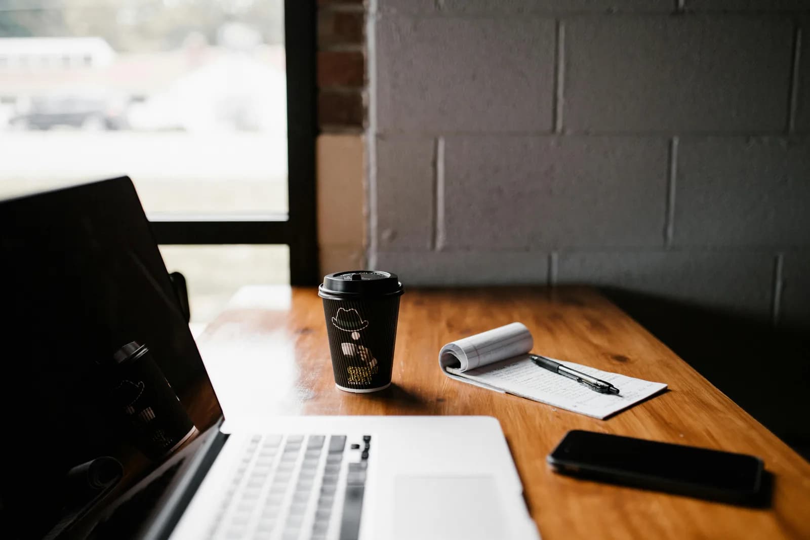 A laptop and a cup of coffee on a wooden desk by a window, the everyday writing spot of a blogger
