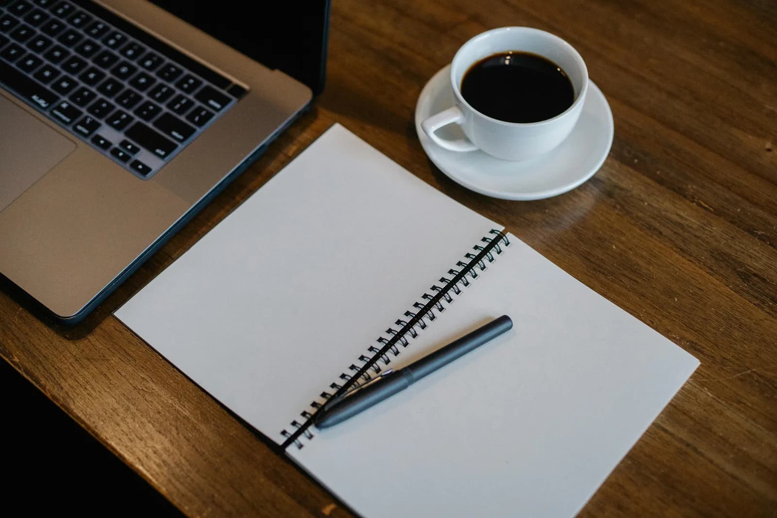 Laptop, notepad, and coffee on a clean office desk, suggesting a consultant drafting between meetings
