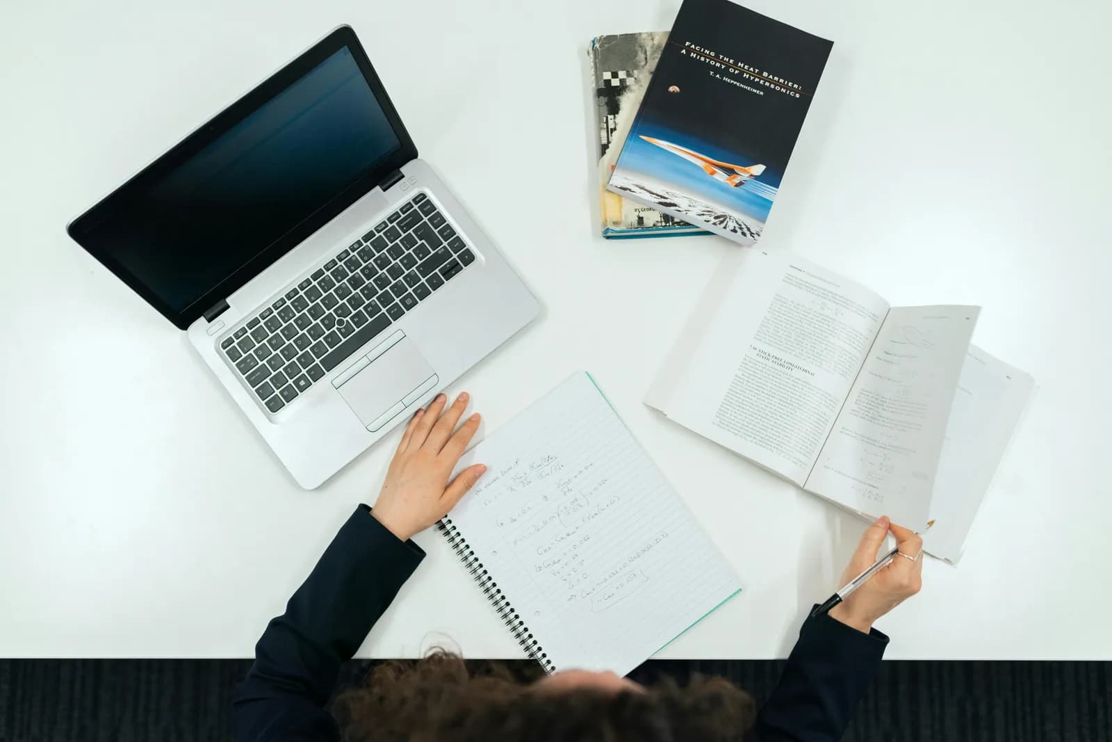 Student studying with a laptop and notebook at a desk, evoking essay writing and note-taking