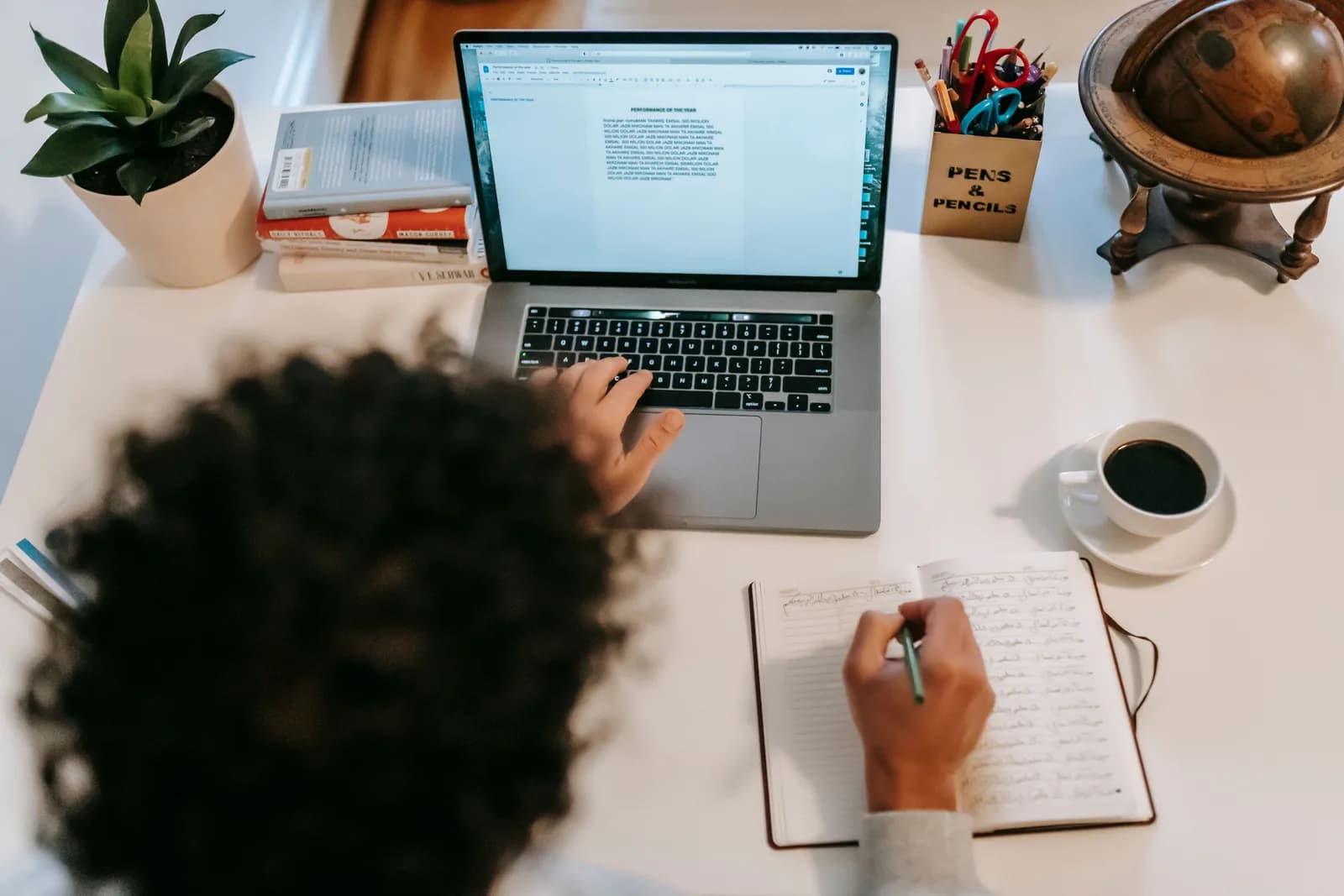 Open notebook, pen, and coffee on a wooden writing desk beside a laptop, evoking long-form drafting