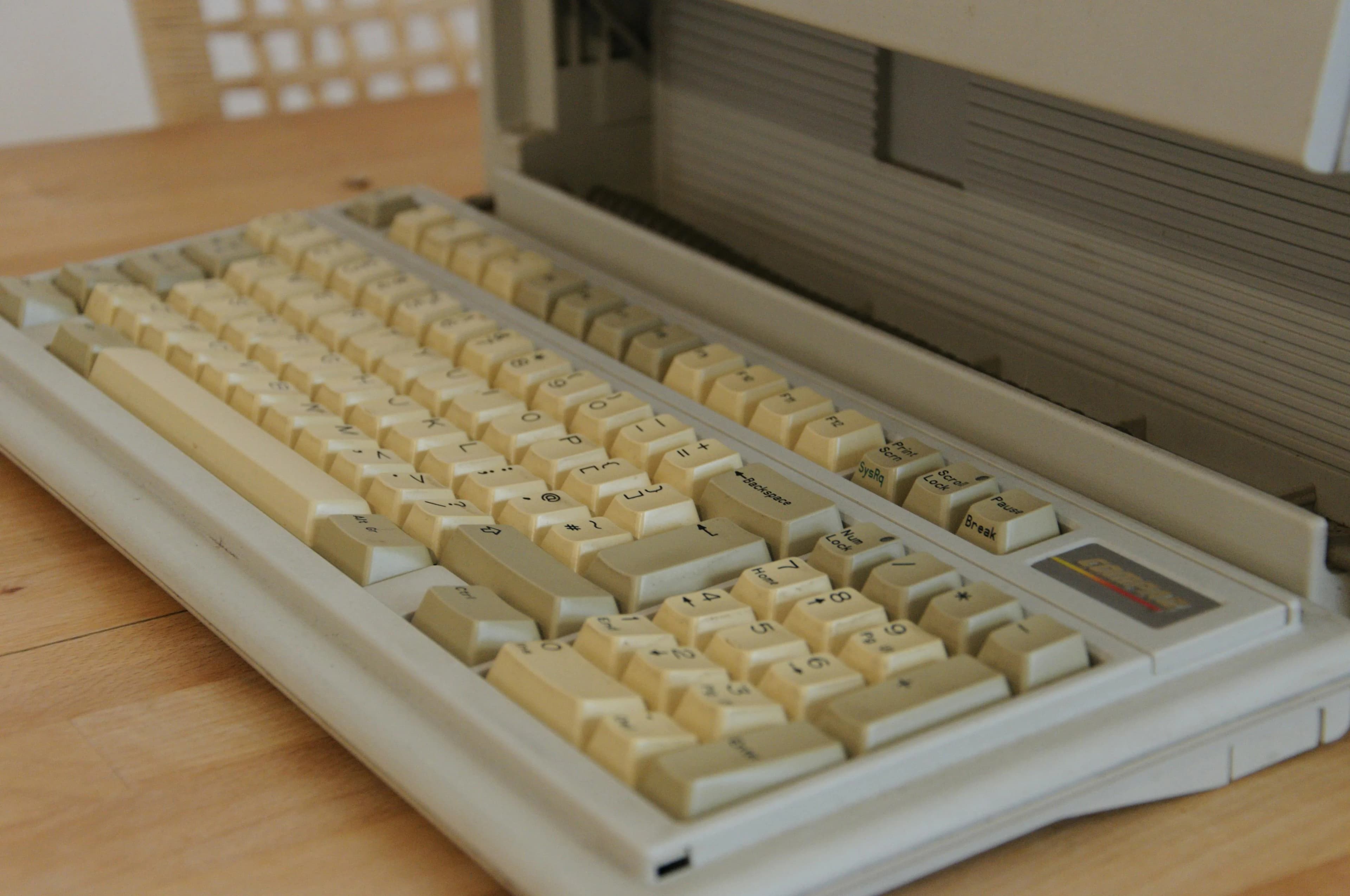 Vintage computer keyboard with yellowed keys on a wooden desk, evoking aging dictation software