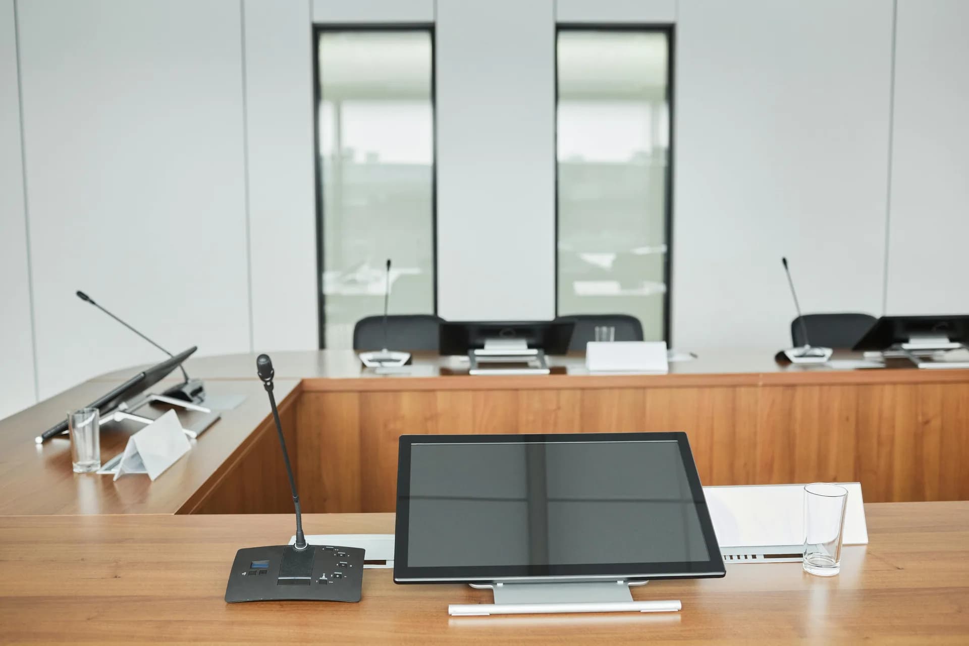 Empty conference room with microphones and monitors on a wooden table, set up for recorded meetings