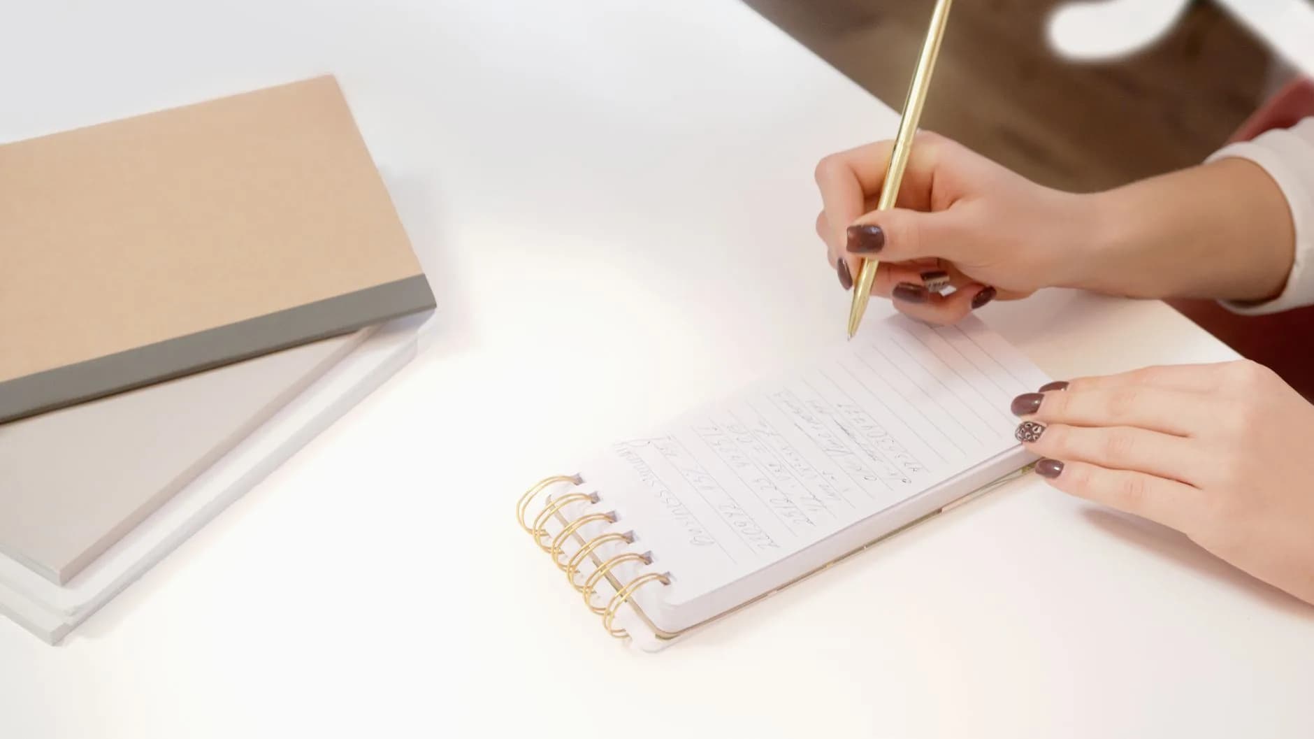 Close-up of hands writing in a spiral notebook on a white desk, evoking manual transcription