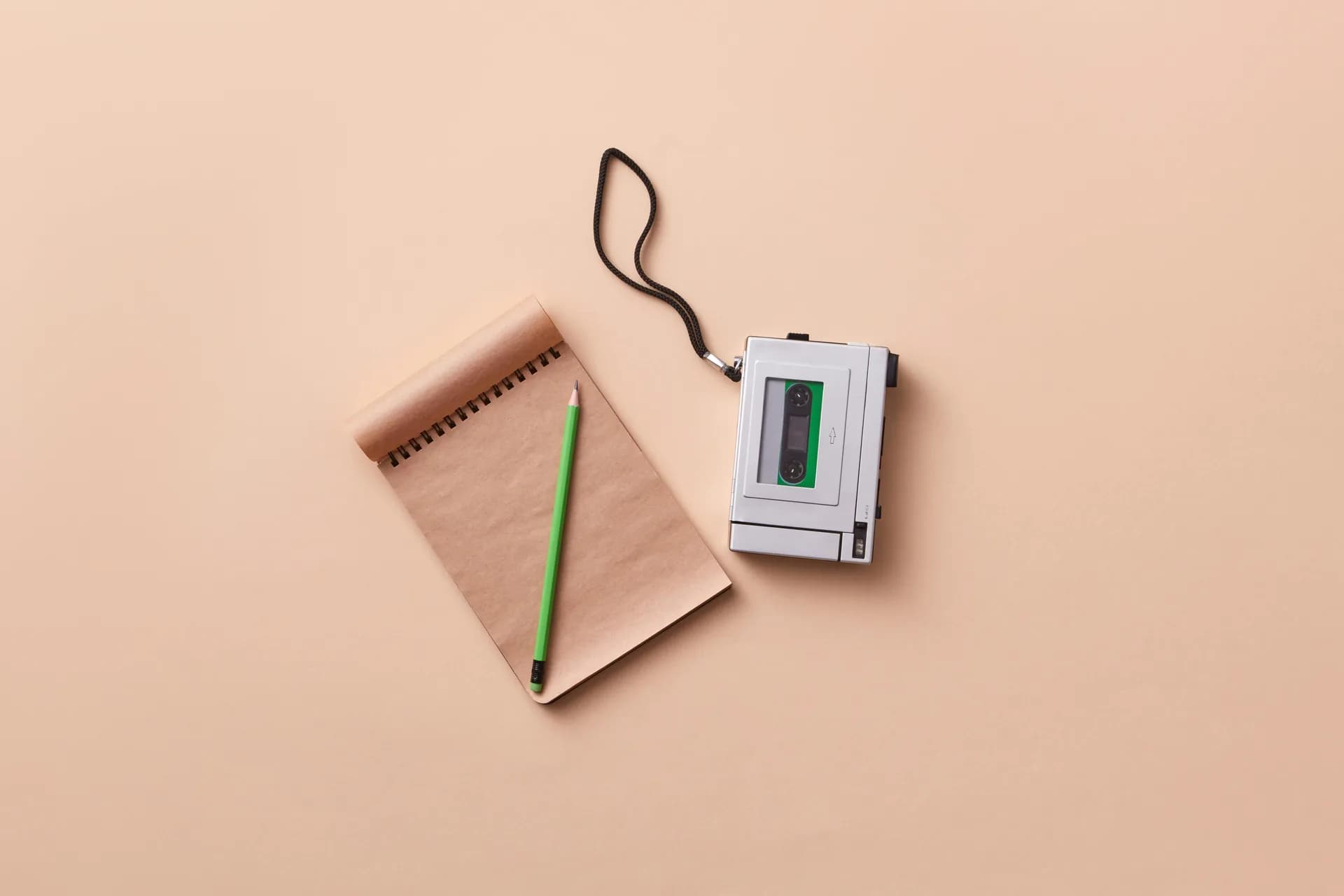Top-down view of a handheld voice recorder beside a spiral notebook and pencil on a plain desk