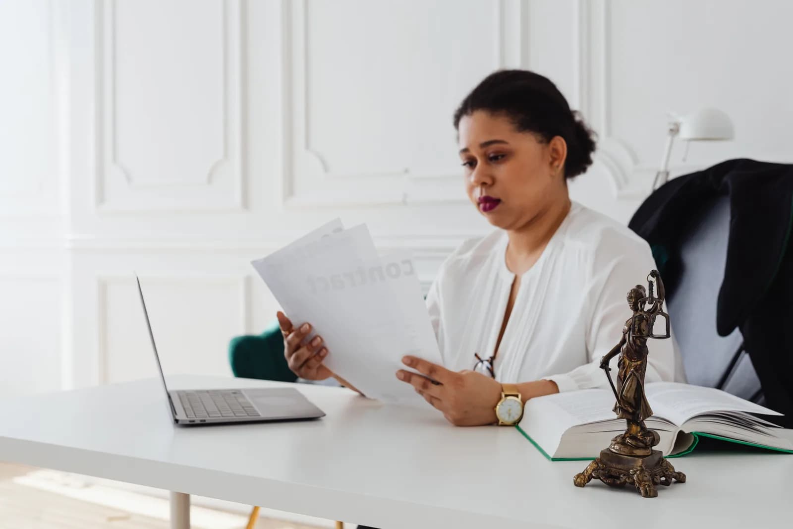 Law books, a notepad, and a laptop on a wooden desk in a quiet office, evoking legal drafting
