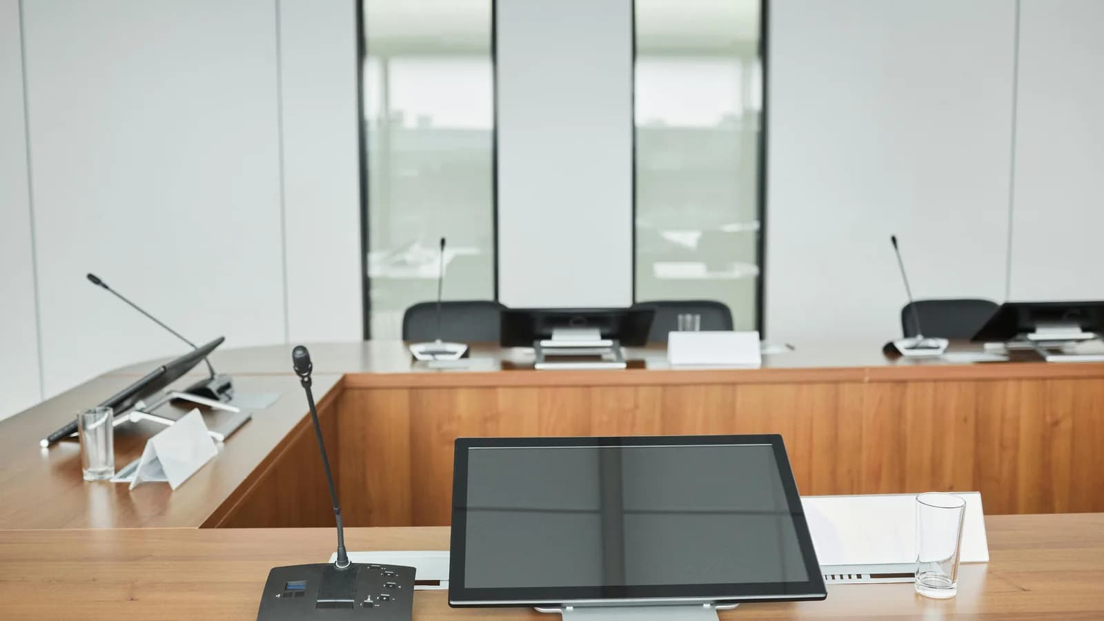 Empty conference table lined with microphones and monitors, set for a meeting that software will transcribe