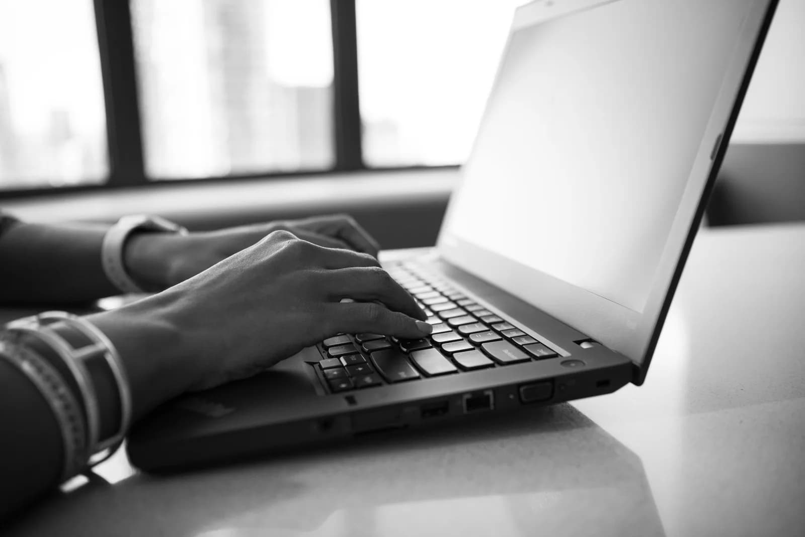 Black-and-white close-up of hands typing on a laptop, suggesting the friction of copy-pasting text between apps