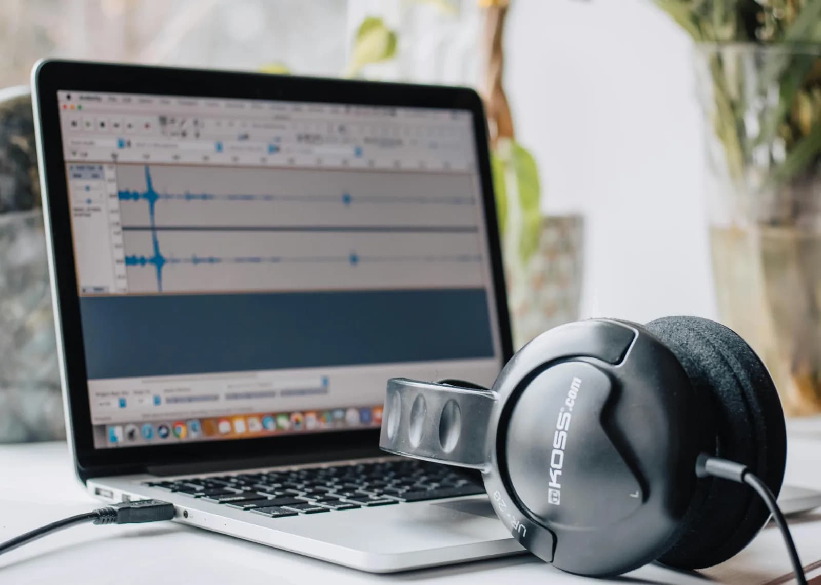 Laptop running audio editing software with headphones on a desk in a home workspace