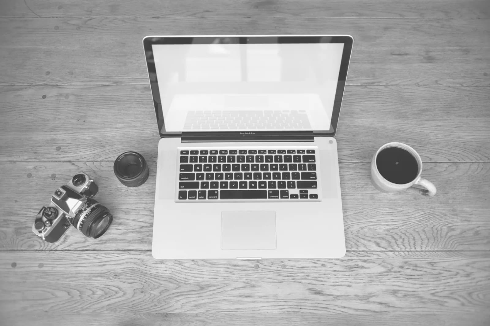 A Mac on a wooden desk beside a coffee and a notebook, evoking calm markdown note-taking