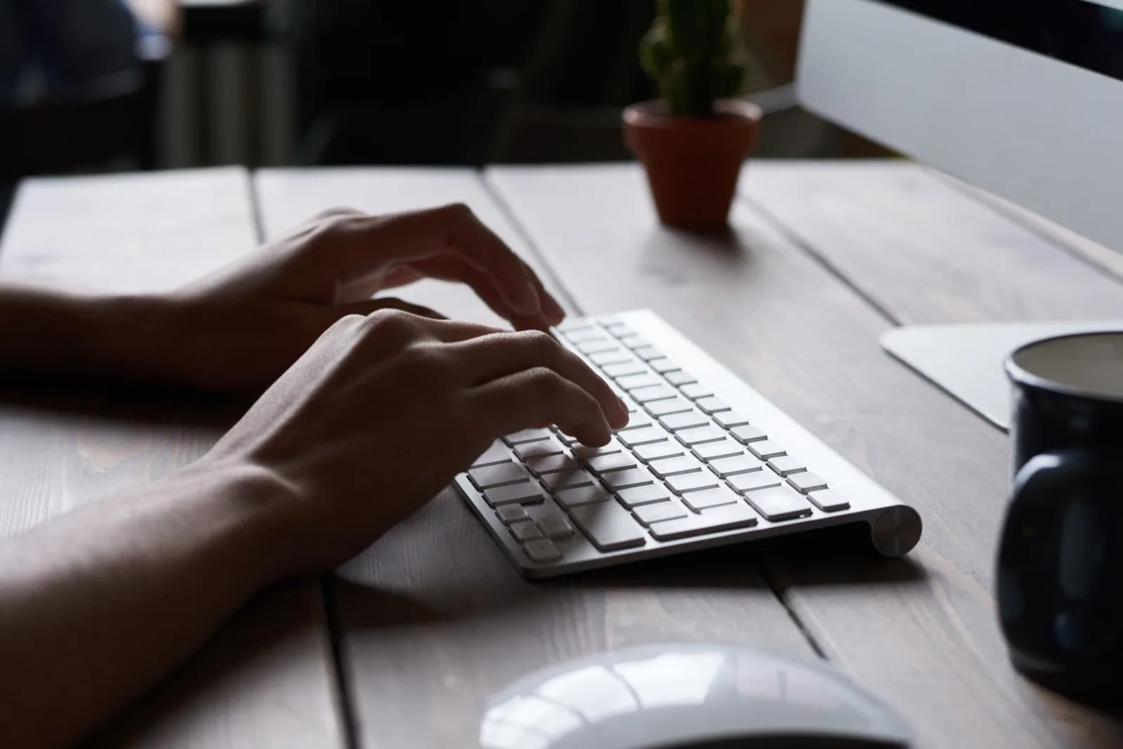 Hands resting on a Mac keyboard beside a phone, illustrating the choice between typing and talking