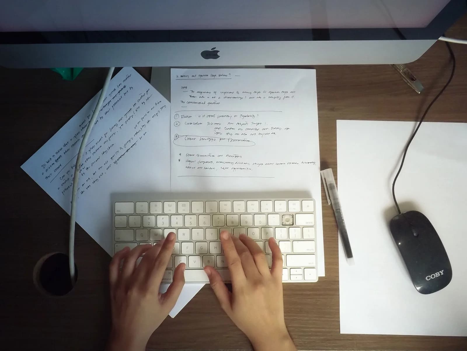 Hands typing on a keyboard at a wooden desk with papers and a mouse, the usual way of entering text into a task tool