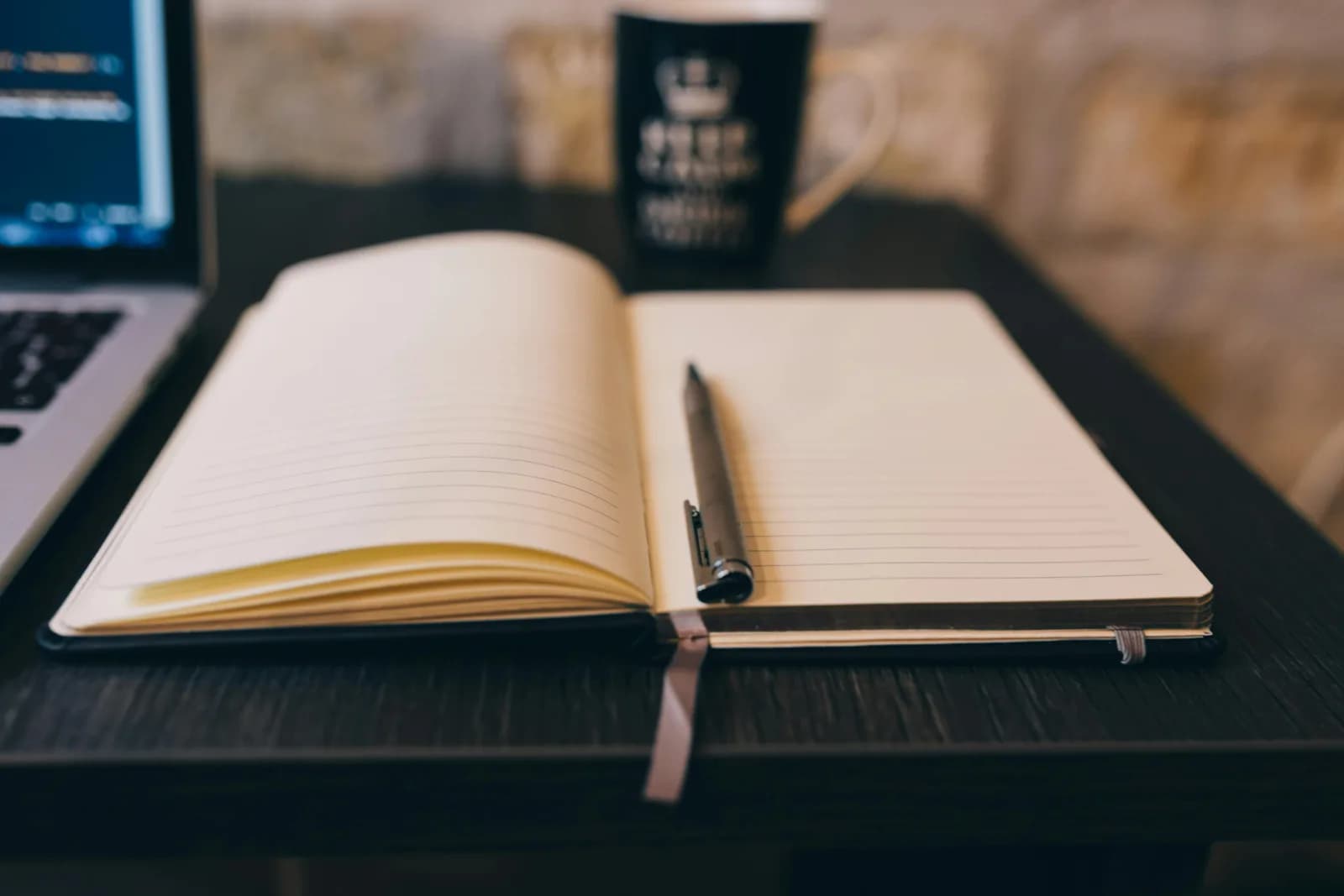 Open notebook with a pen beside a laptop and a mug in a cozy setting, weighing built-in note tools