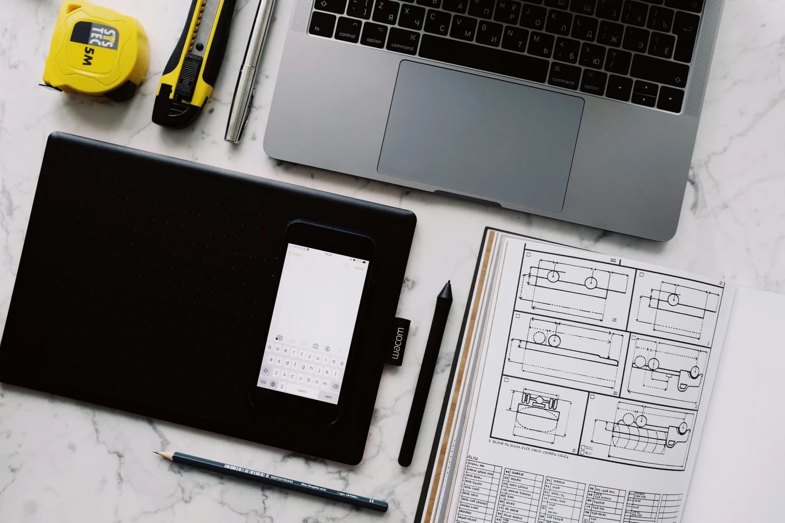 Overhead view of a desk with gadgets, a notebook, and sketching tools side by side