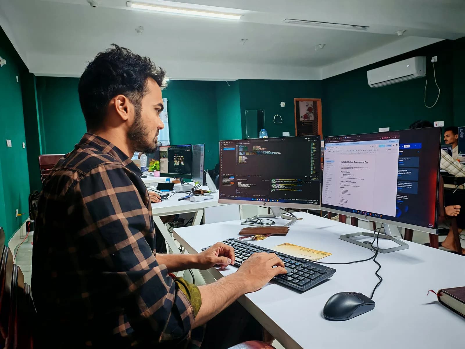 Developer working on code at a dual-monitor setup in a modern office