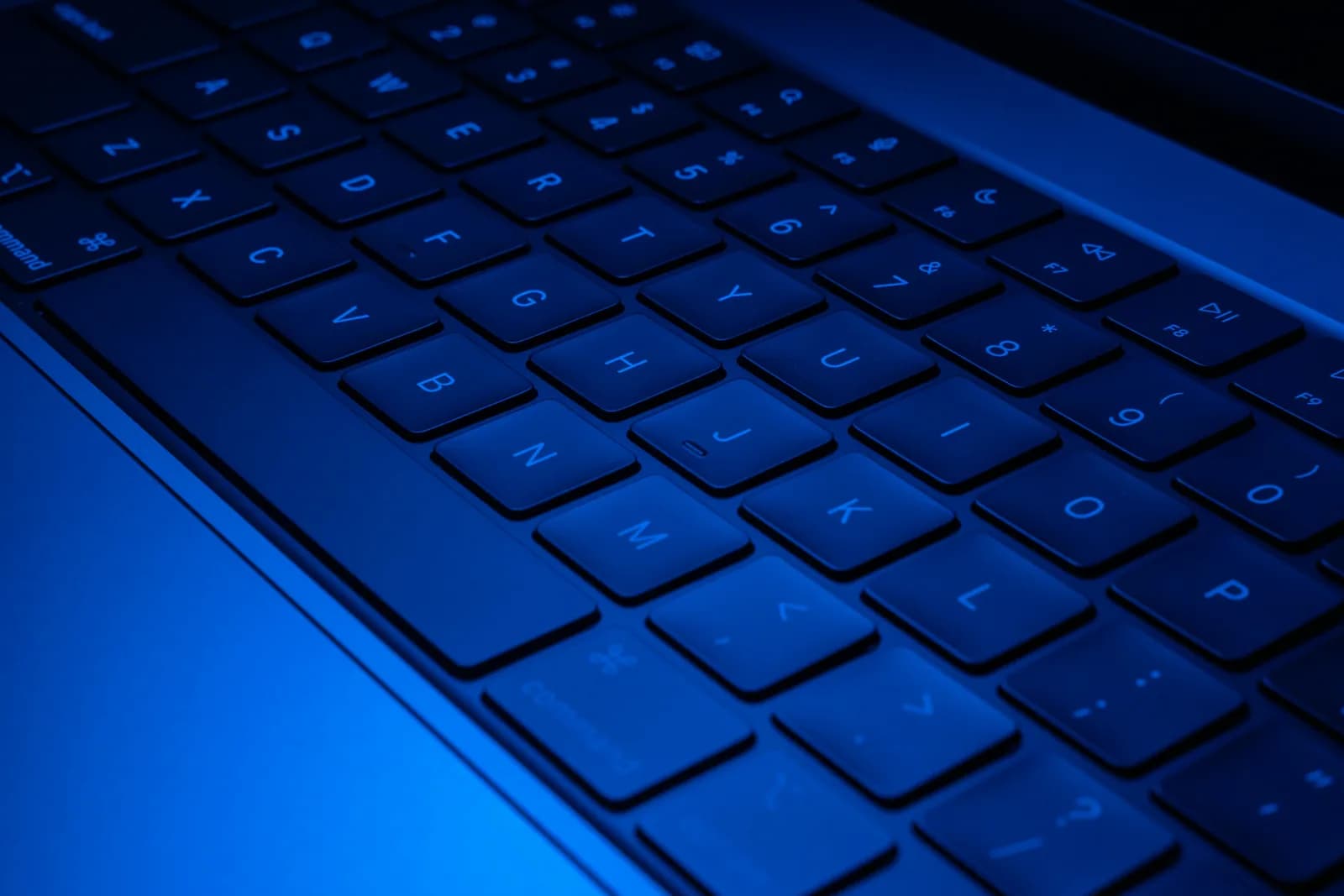 Close-up of a laptop keyboard illuminated with blue light, evoking hands-on coding