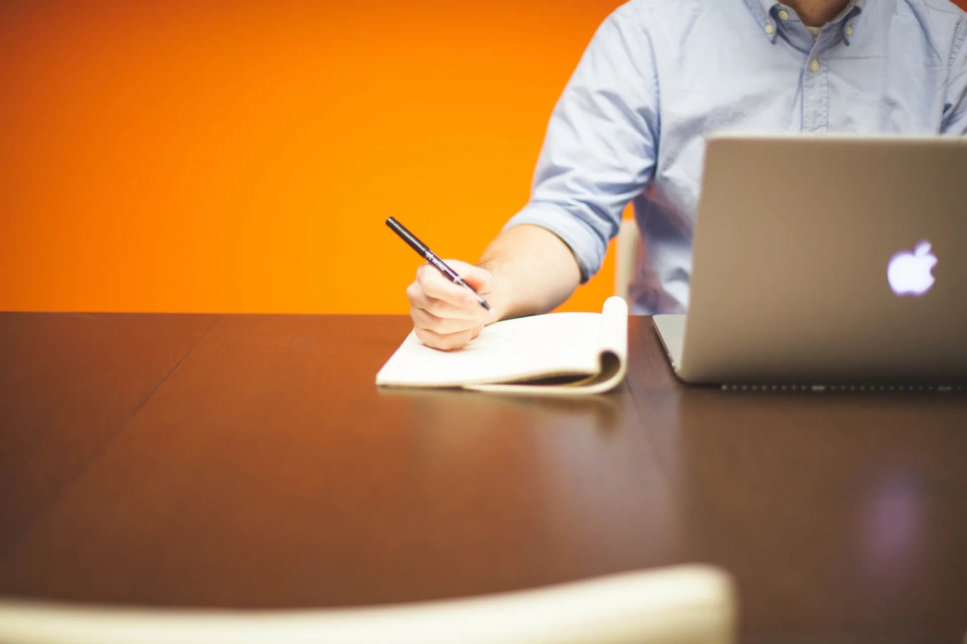 Open notebook with a pen beside a laptop on a wooden desk, capturing notes by hand and on screen