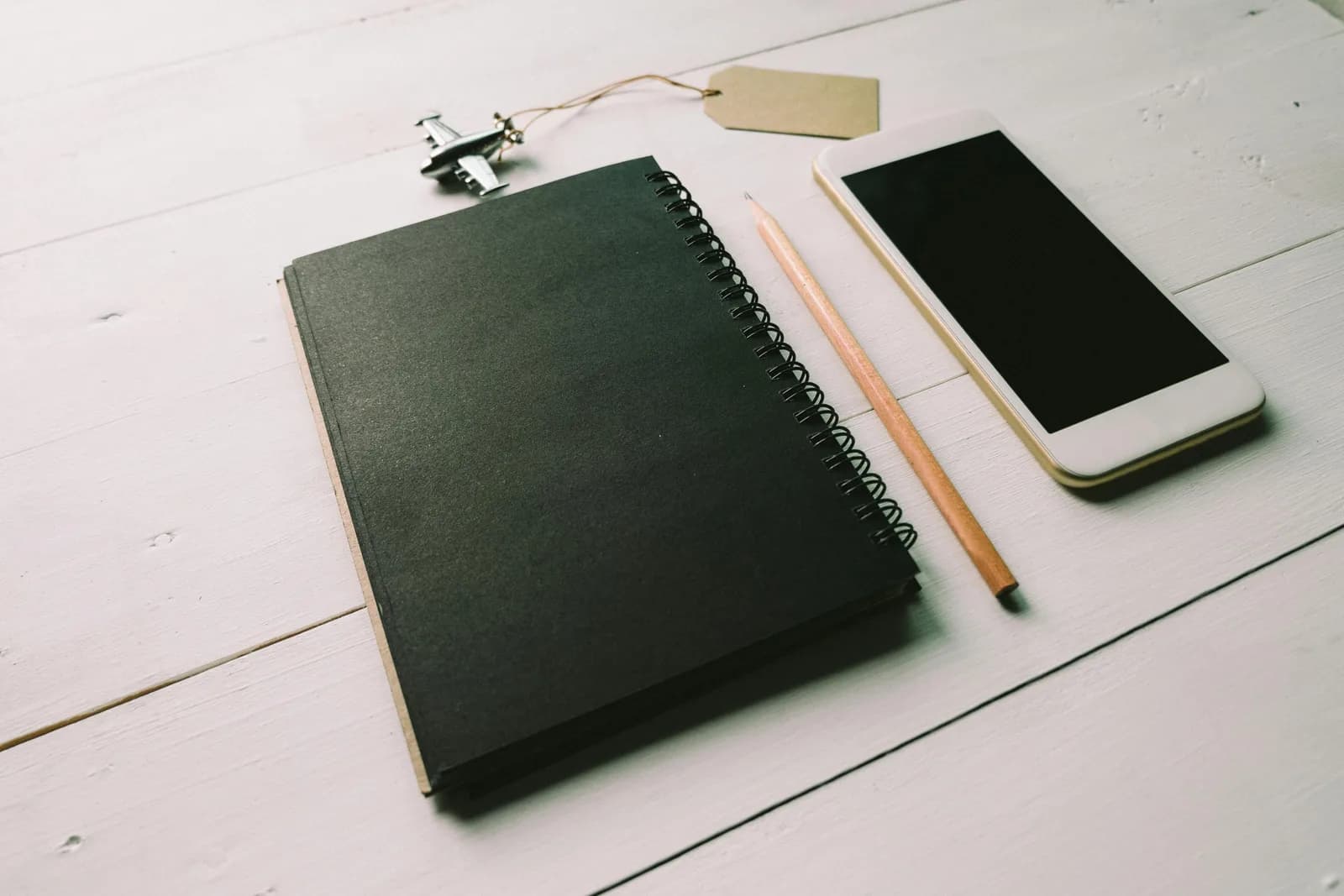 Flat lay of a black spiral notepad, smartphone, and pencil on a light desk for mobile note-taking