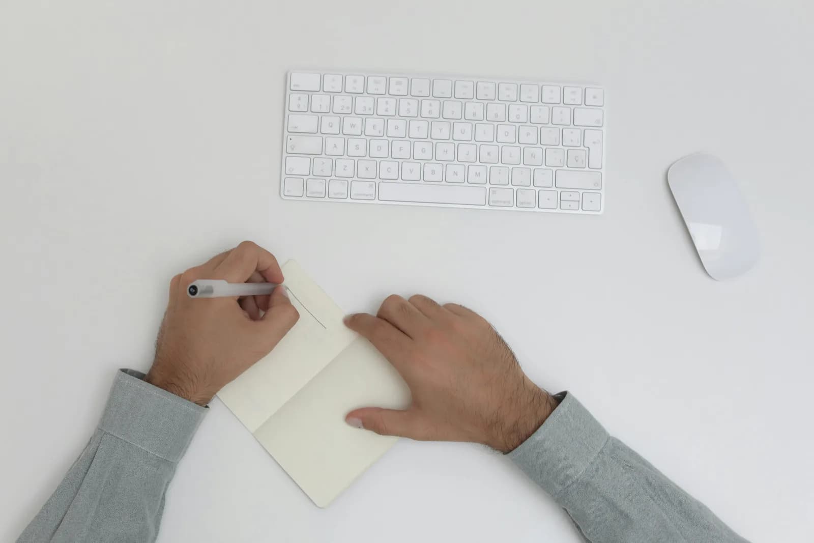 Hands writing in a paper notebook beside a keyboard, contrasting typing with dictation