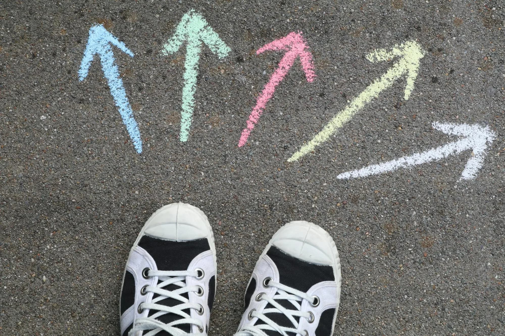 Scarpe da ginnastica sull'asfalto tra frecce di gesso che puntano in due direzioni, a illustrare la scelta di uno strumento