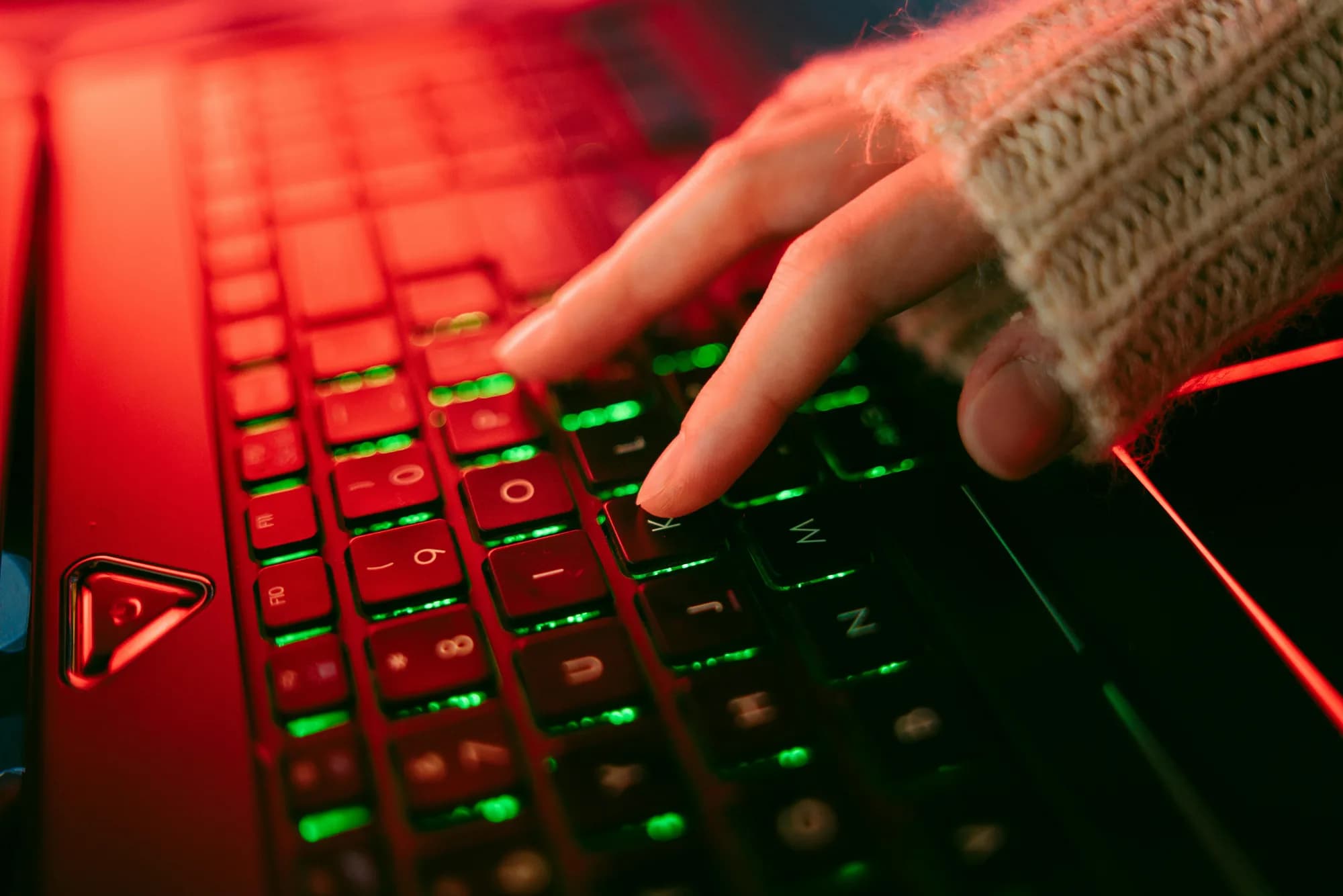 Hand on a backlit keyboard in dim ambient light, evoking the press-a-key moment that triggers Windows Voice Typing