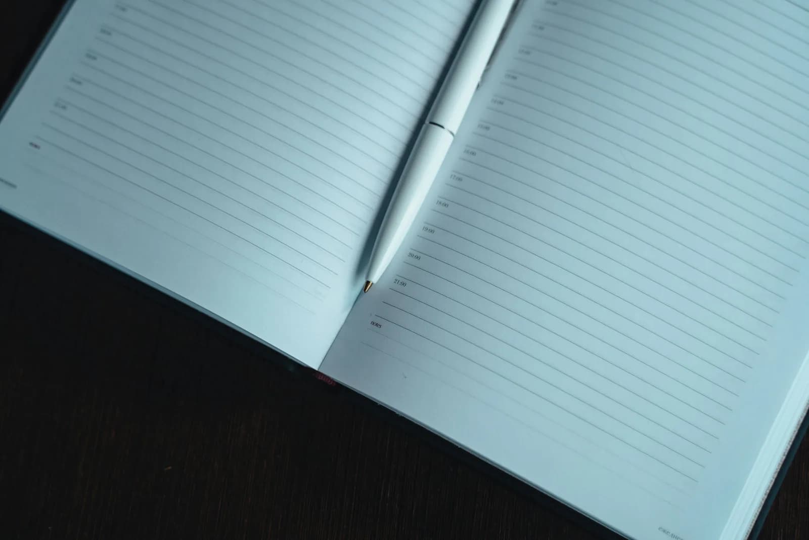 Open notebook and pen beside a laptop on a dark desk, evoking networked note-taking and dictation
