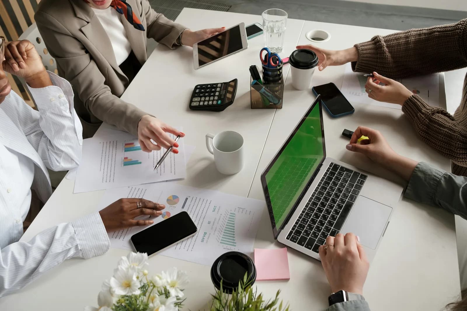 Top view of a sales team's hands at a desk with charts and a laptop, weighing which CRM tools fit
