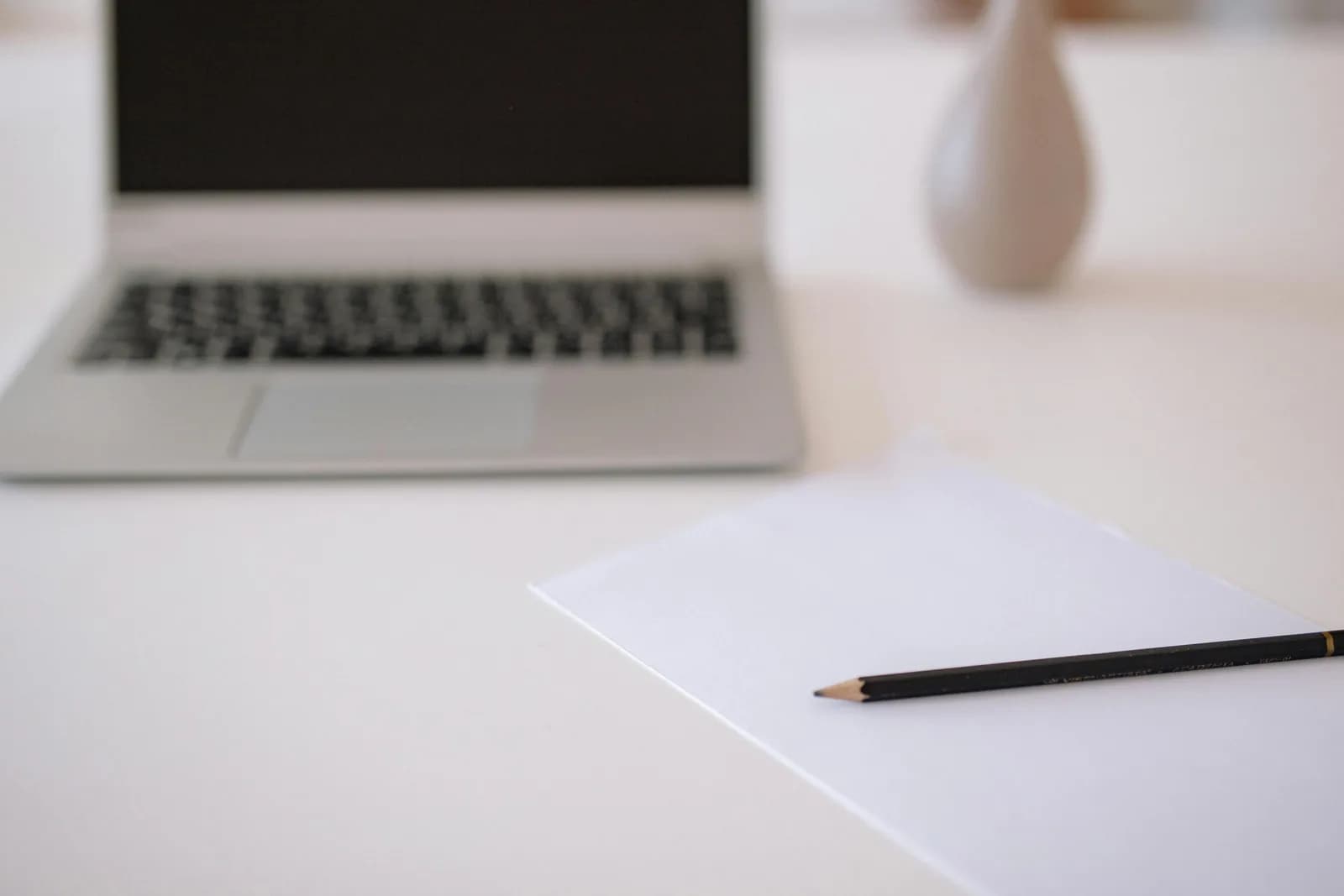 A minimal workspace with a laptop, blank paper and pencil on a white table, weighing the simpler path