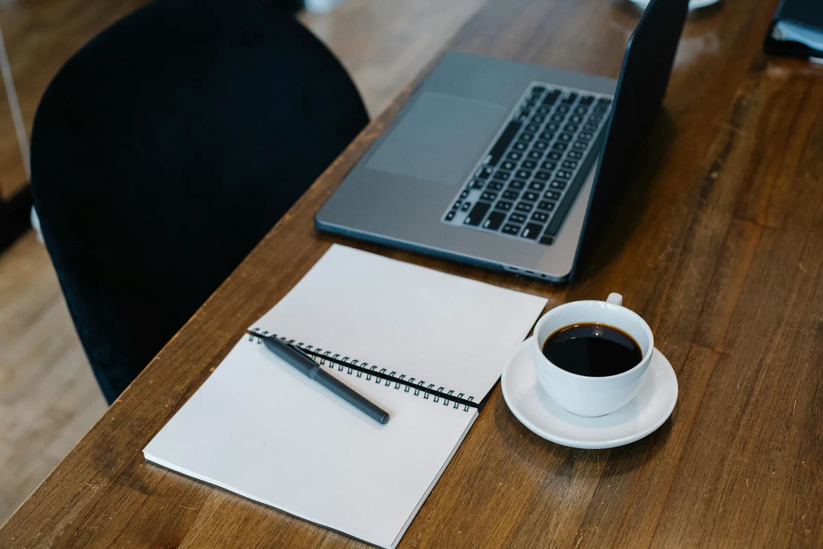 High-angle view of an open laptop beside a blank spiral notebook, contrasting live captions with a saved transcript