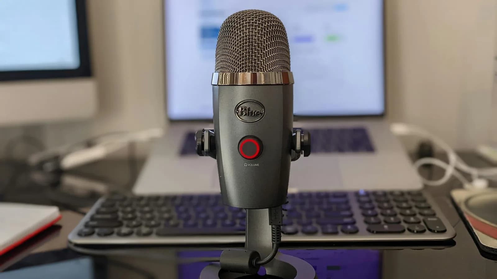Microphone in focus with a blurred keyboard and laptop in a home office, a voice-over-typing setup