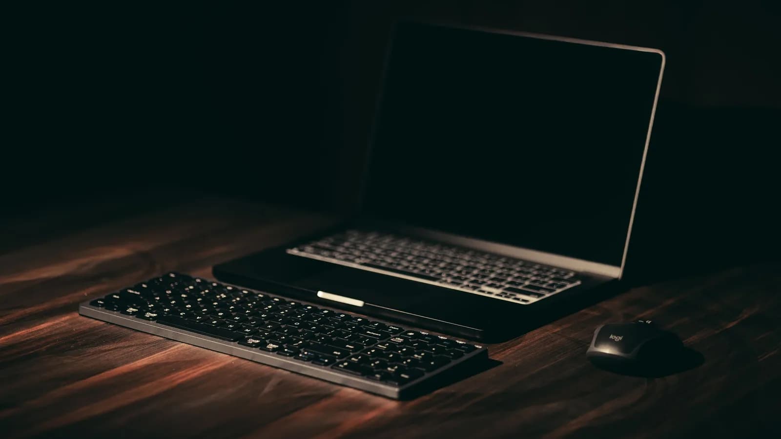 A dark, minimalist desk with a laptop and keyboard, lit low for late-night writing