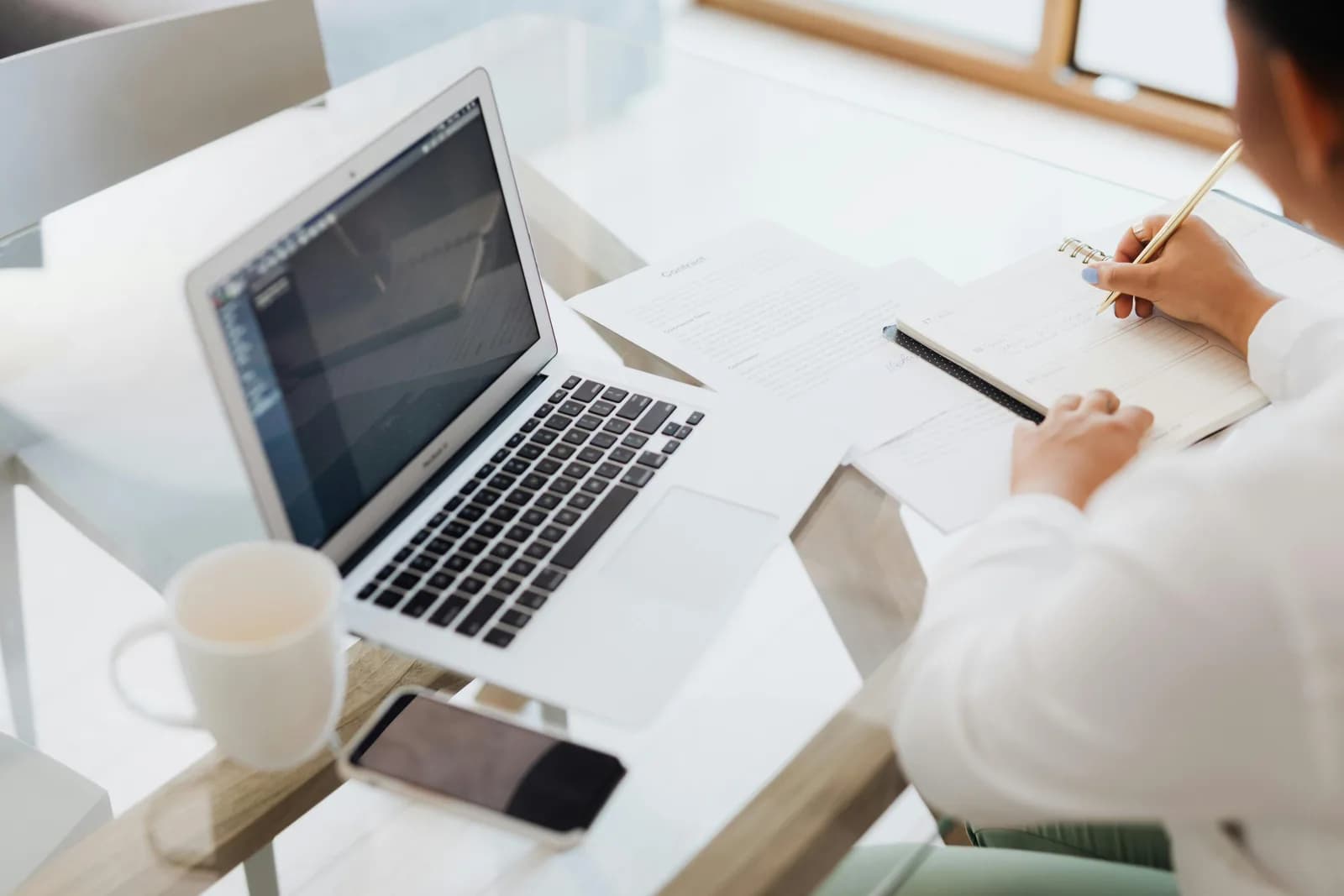 A person typing at a laptop with a notebook and coffee nearby, mid-draft on a blog post