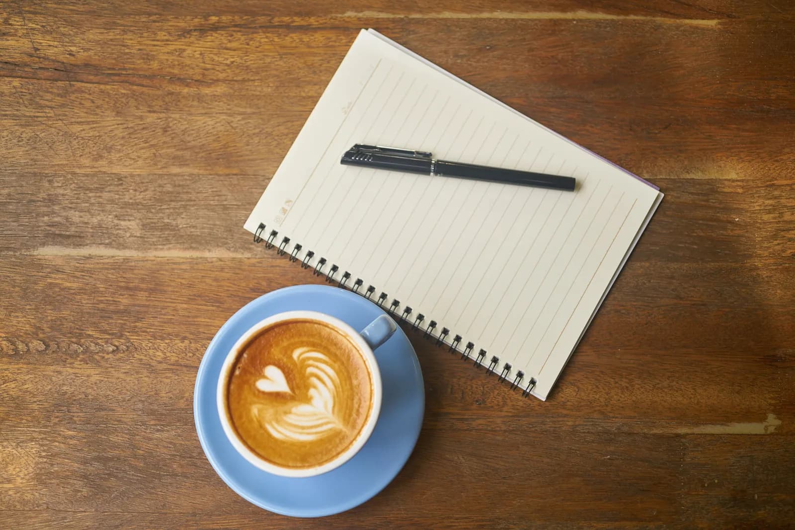 A reporter's spiral notebook, pen and coffee on a wooden desk, suggesting fast note capture