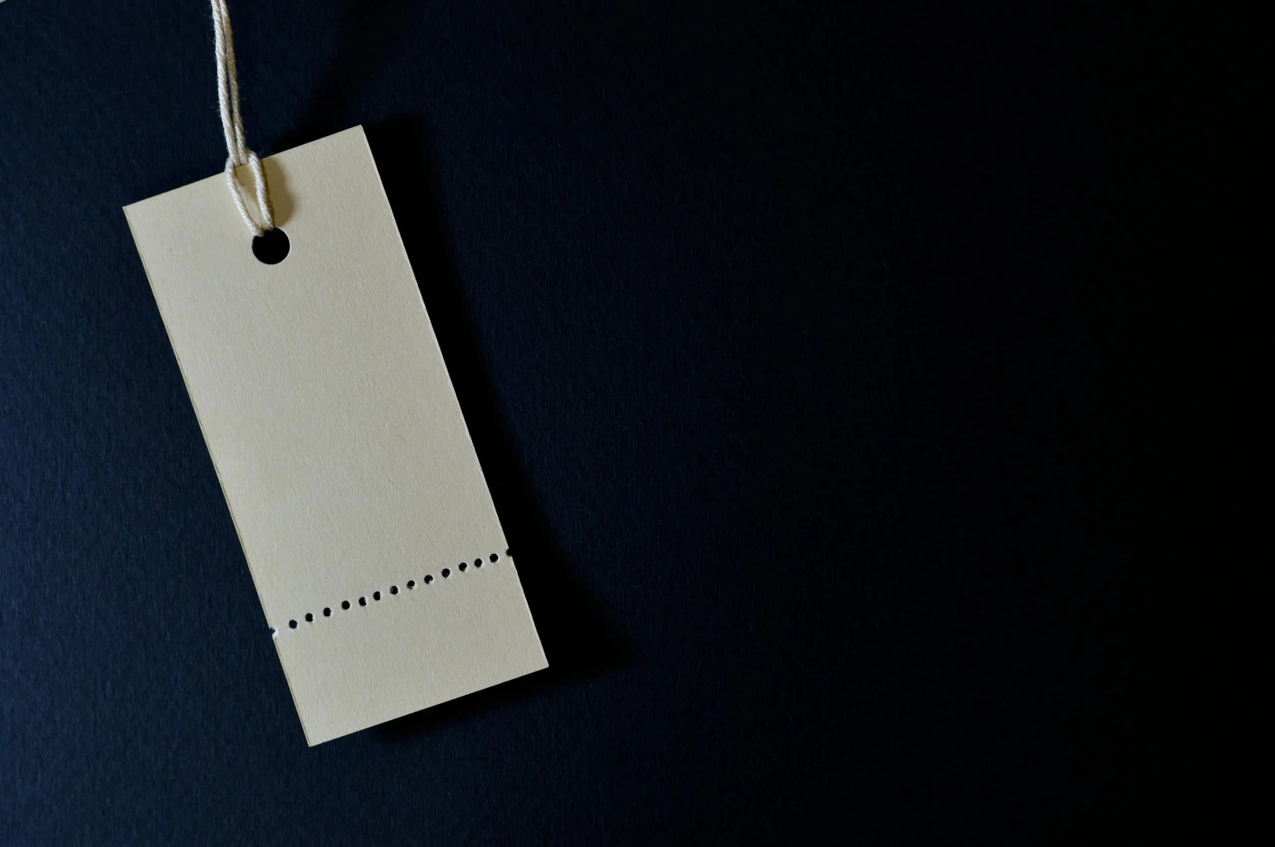 Minimalist blank price tag on a string against a dark background, symbolising a transparent price label