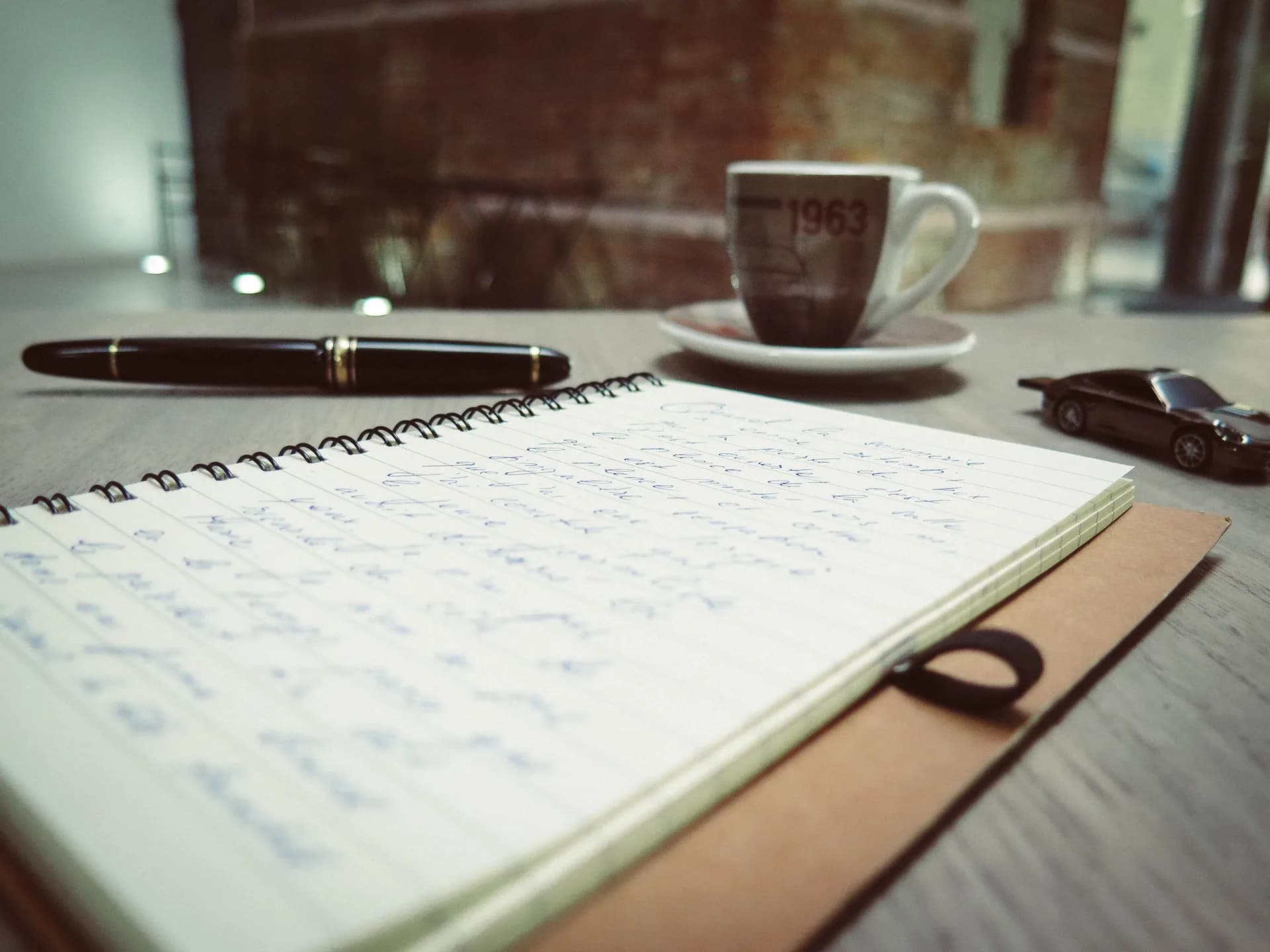 Warm desk with a spiral notepad, blue pen and coffee, set for editing dictated text by hand
