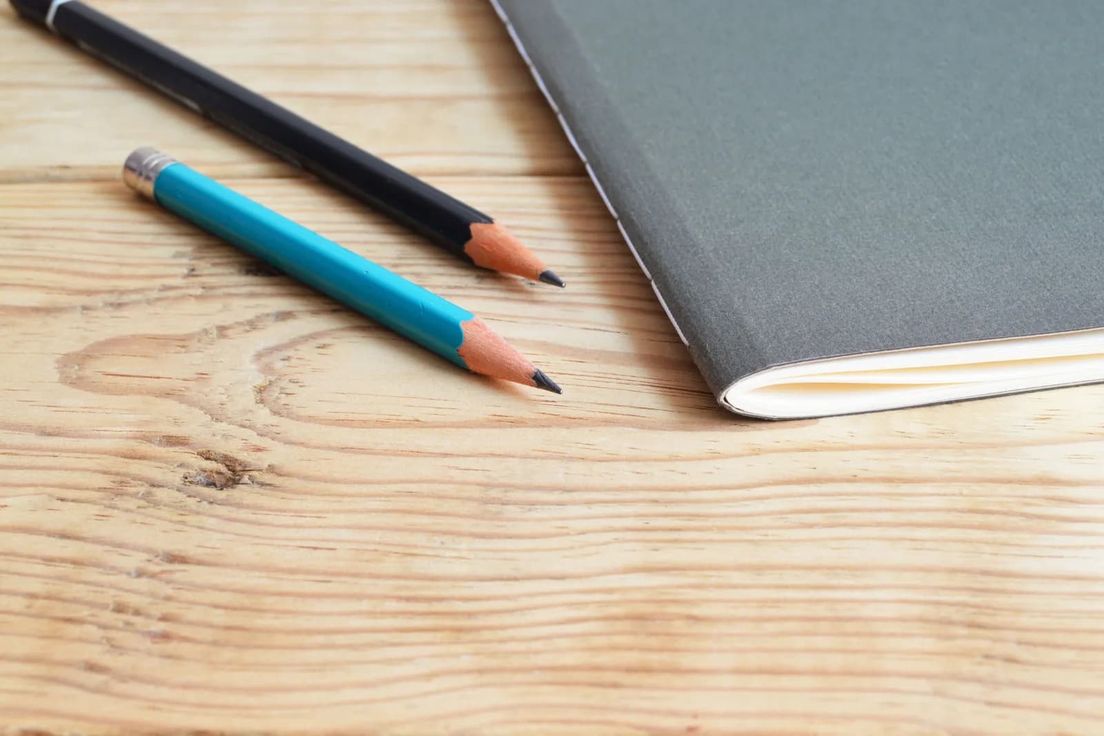 A plain notebook and two pencils on a wooden desk, the moment before anyone starts writing