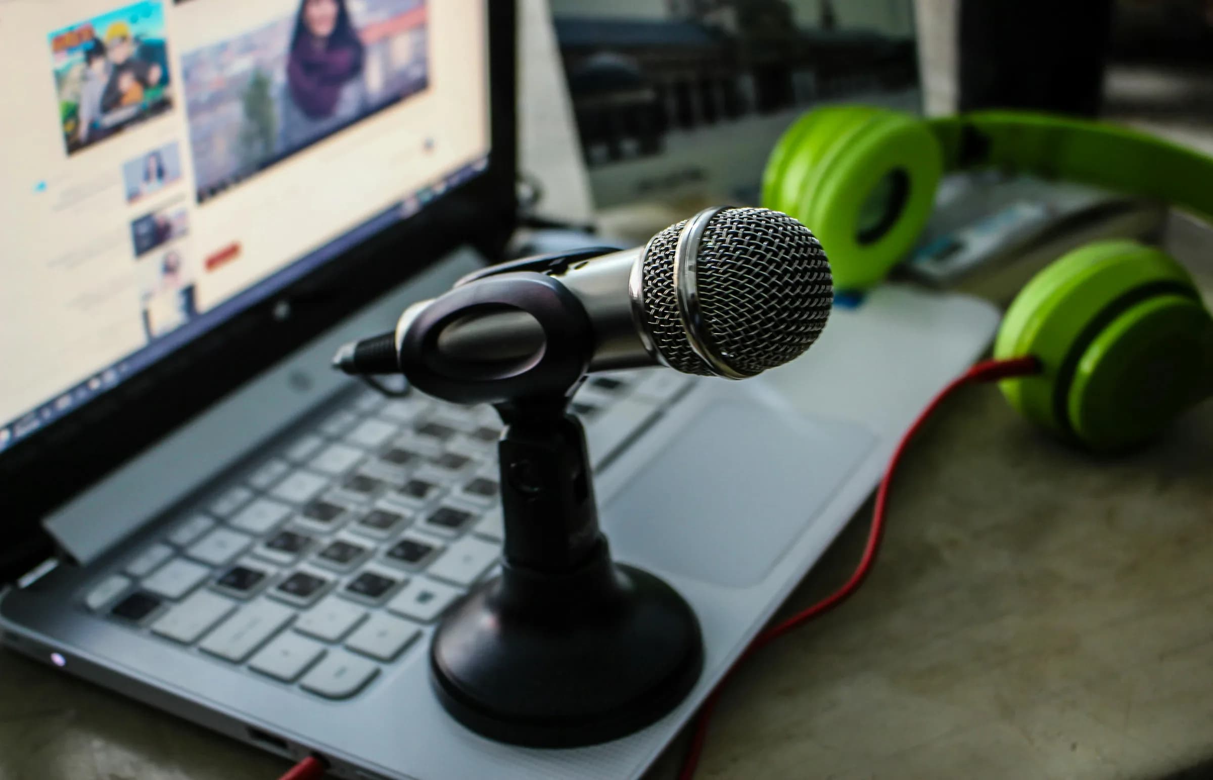 Close-up of a podcasting setup with a condenser microphone, open laptop, and over-ear headphones
