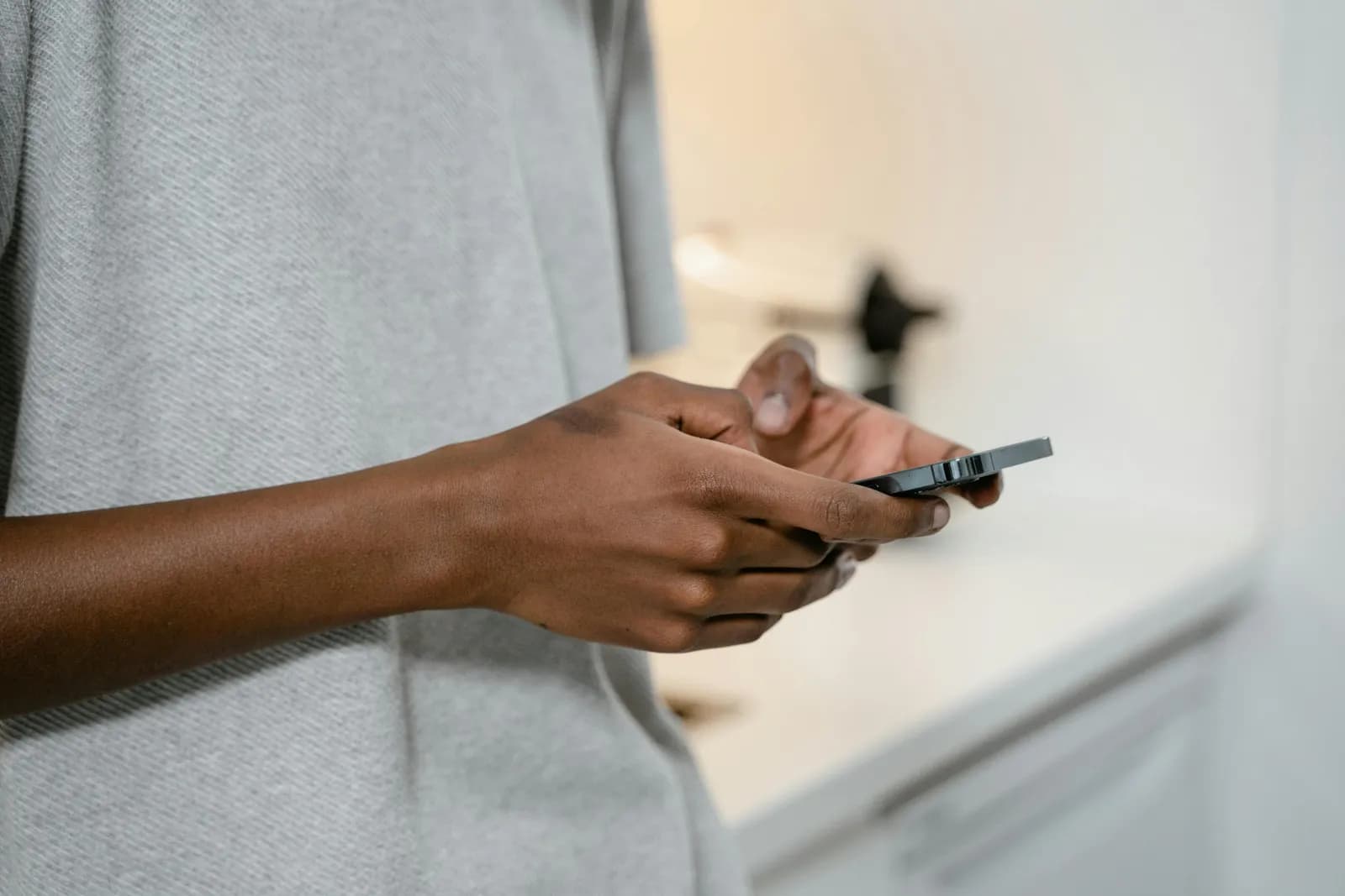 Hands holding a black smartphone indoors, close-up of fingers near the keyboard area