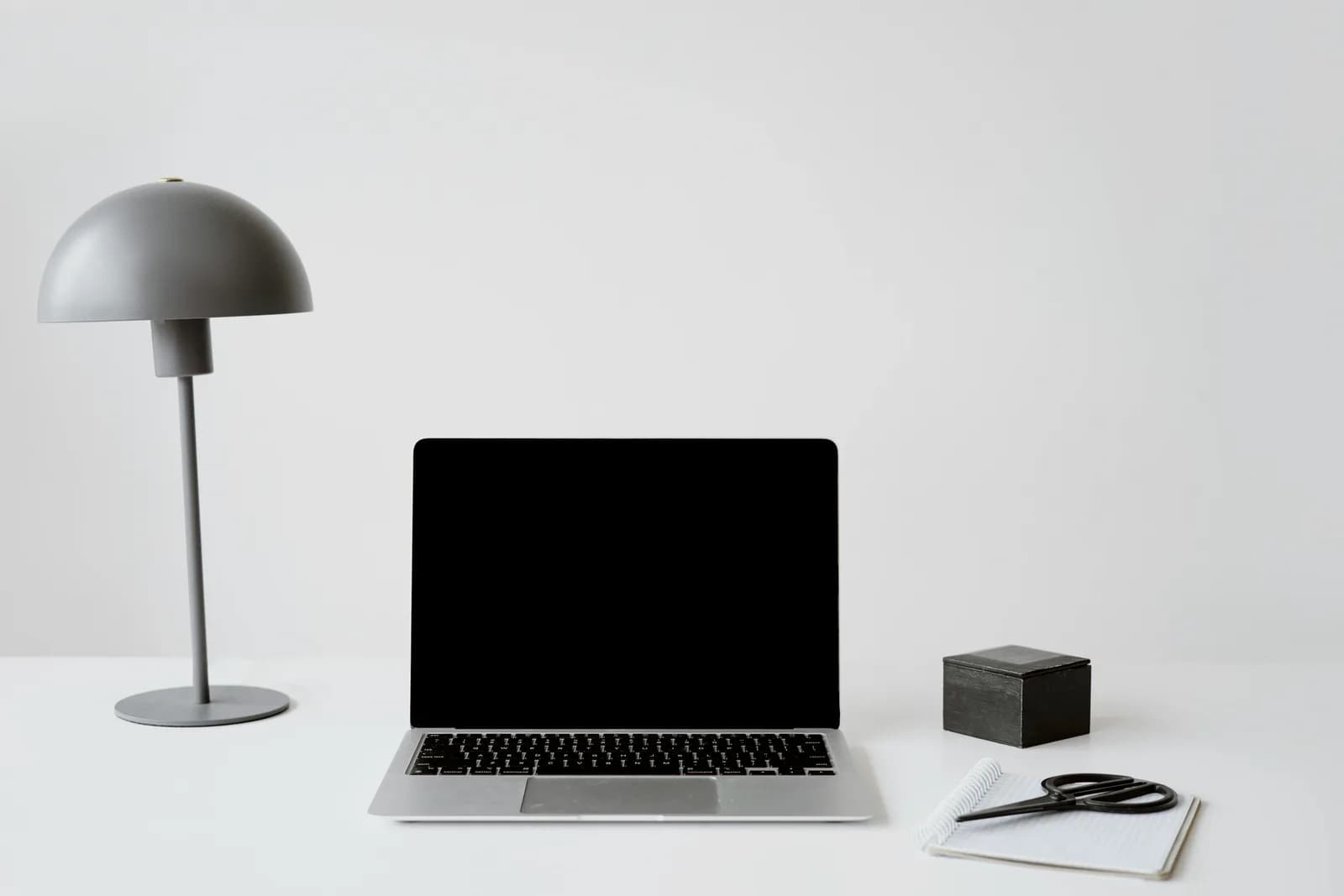 A bright minimalist Mac desk with a closed laptop, a lamp, and a notepad, the setting for dictating notes