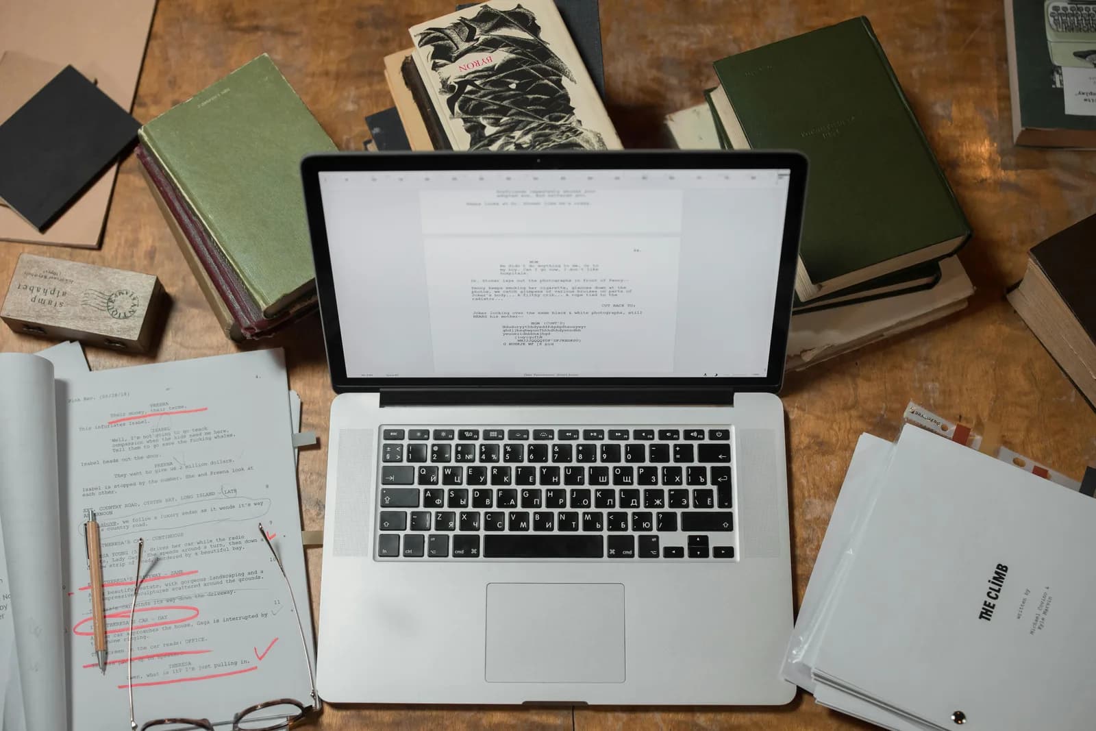 Un laptop e una pila di documenti su una scrivania di legno scuro, che evoca la scrittura di testi lunghi