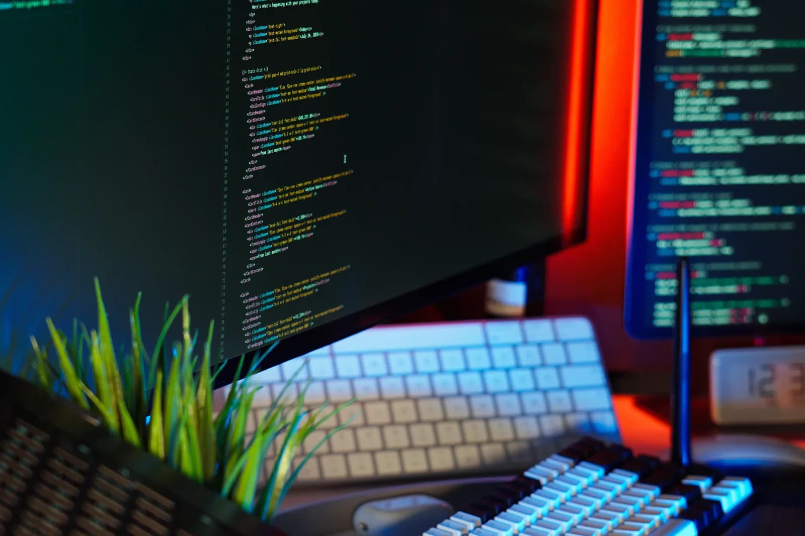 A developer workspace at night with monitors showing source code, a mechanical keyboard, and tech accessories