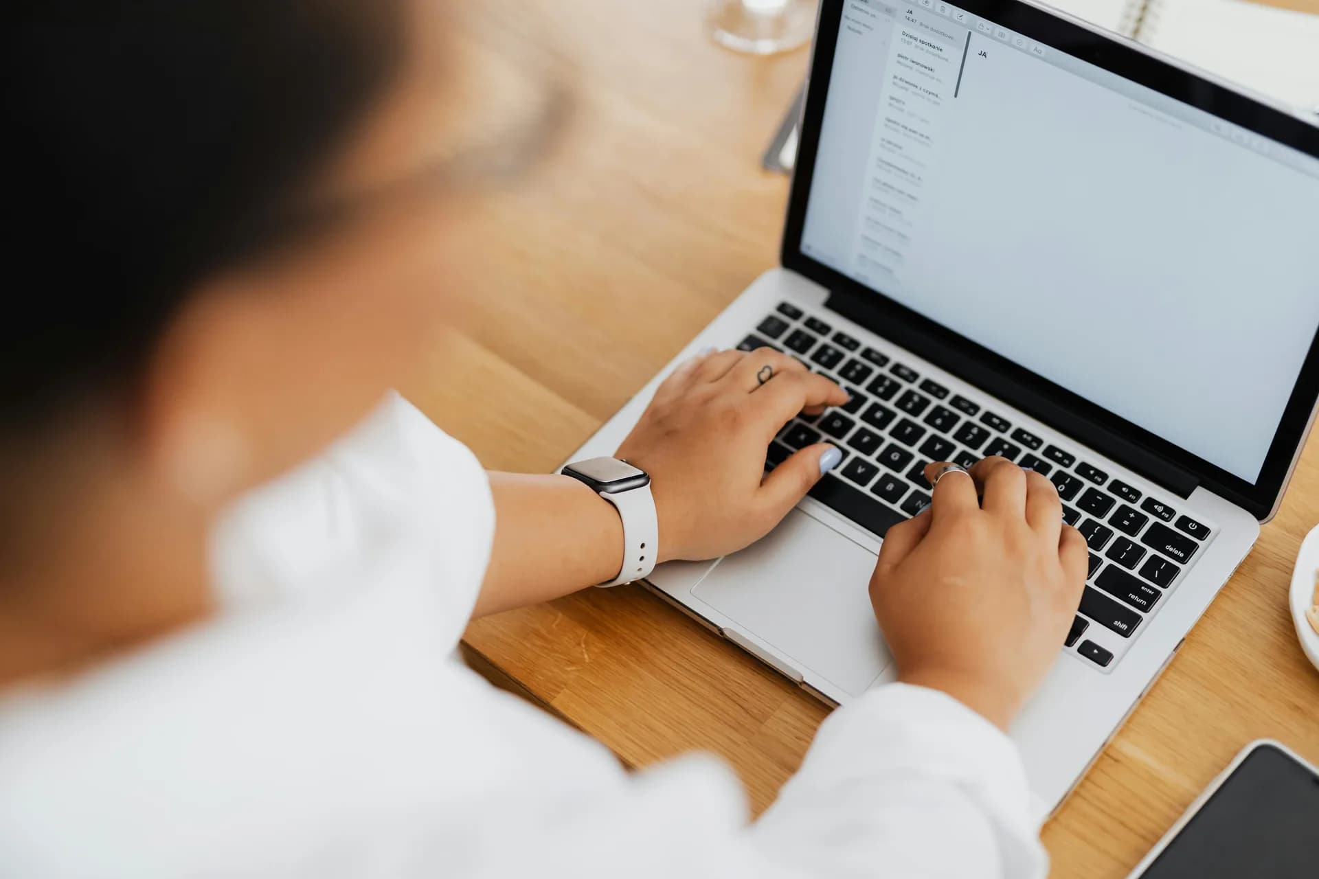 Hands typing on a laptop from above on a clean desk, illustrating the act of writing email at a workstation