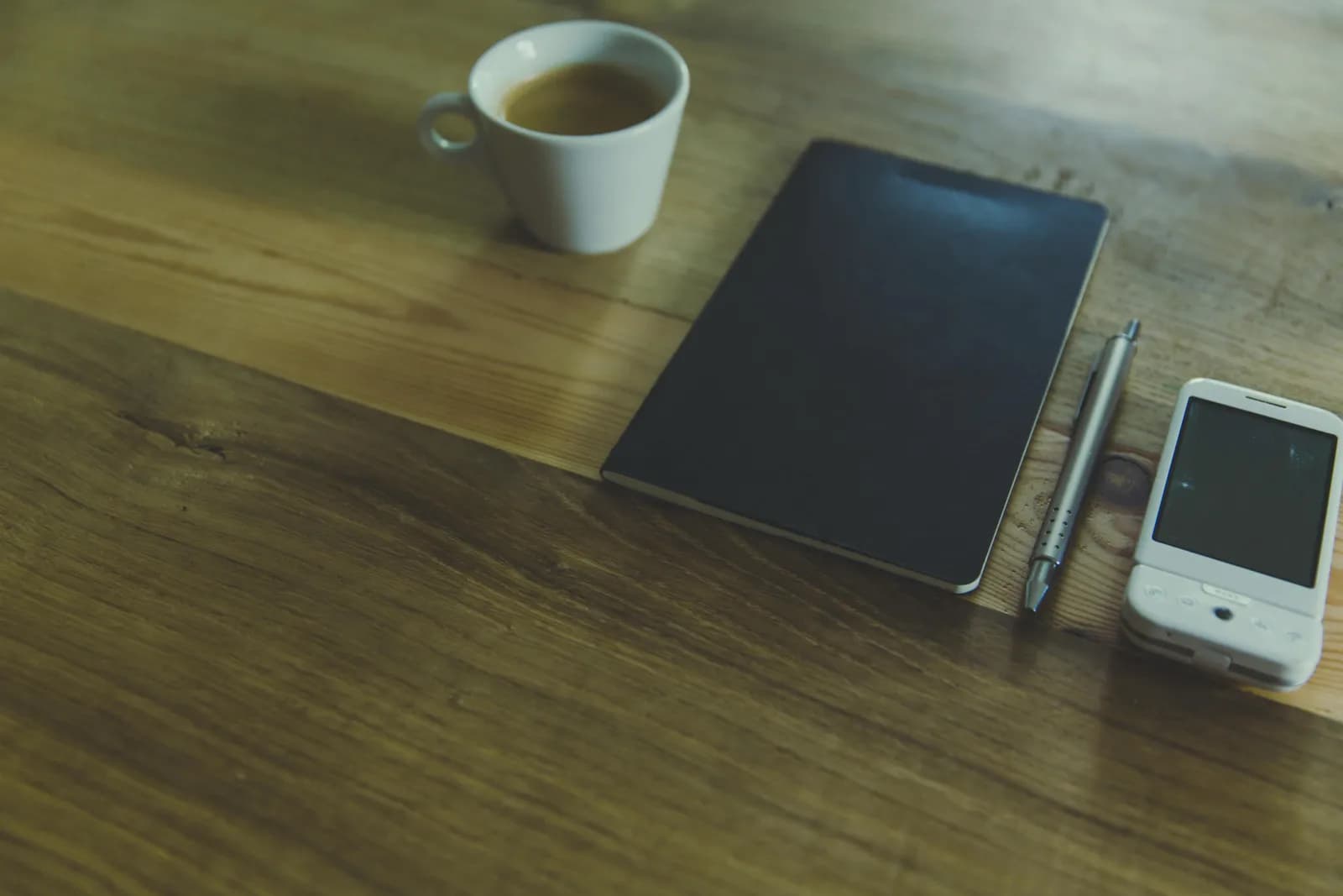 Flat-lay of a smartphone, coffee cup, notebook and pen on a wooden table, evoking mobile email writing