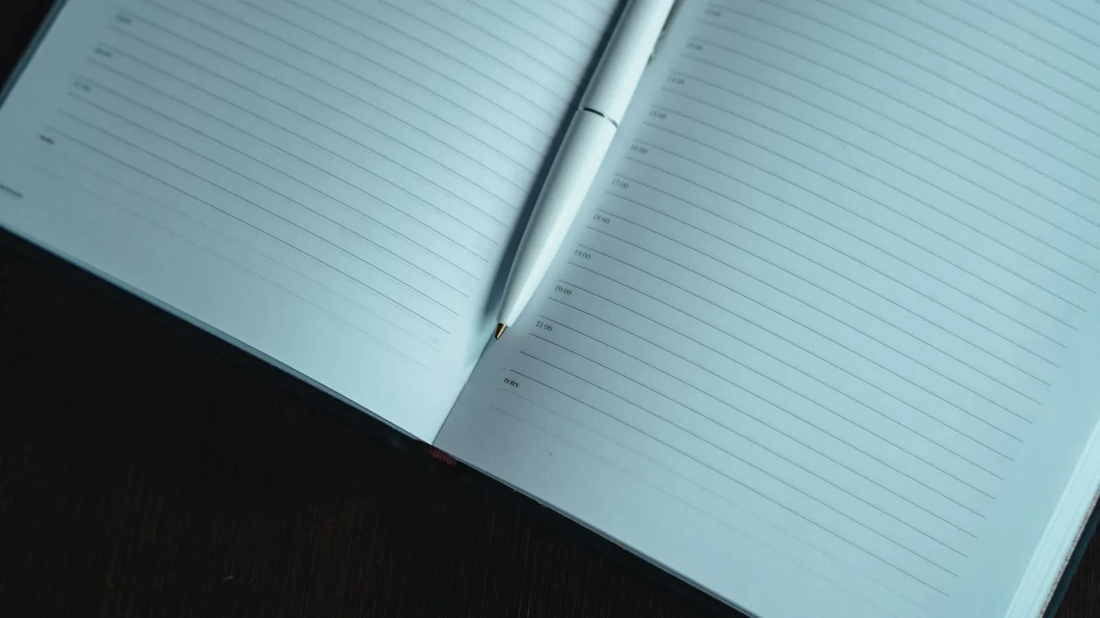 An open notebook with a pen resting on a dark wooden table, lit for quiet evening journaling