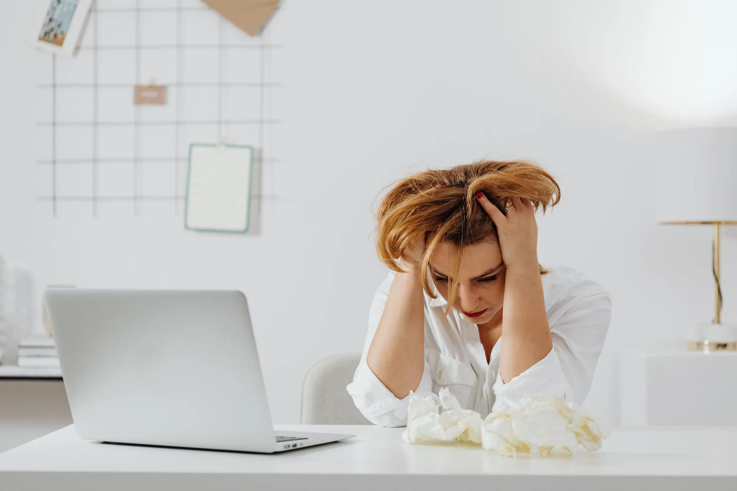 Persona a una scrivania con un laptop, mani sulle tempie, postura che esprime frustrazione di fronte a un'app Windows bloccata