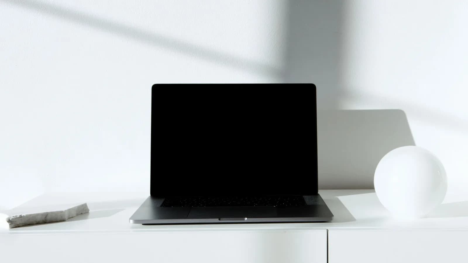 Sleek black laptop on a clean white desk in natural light, a minimal dictation workspace